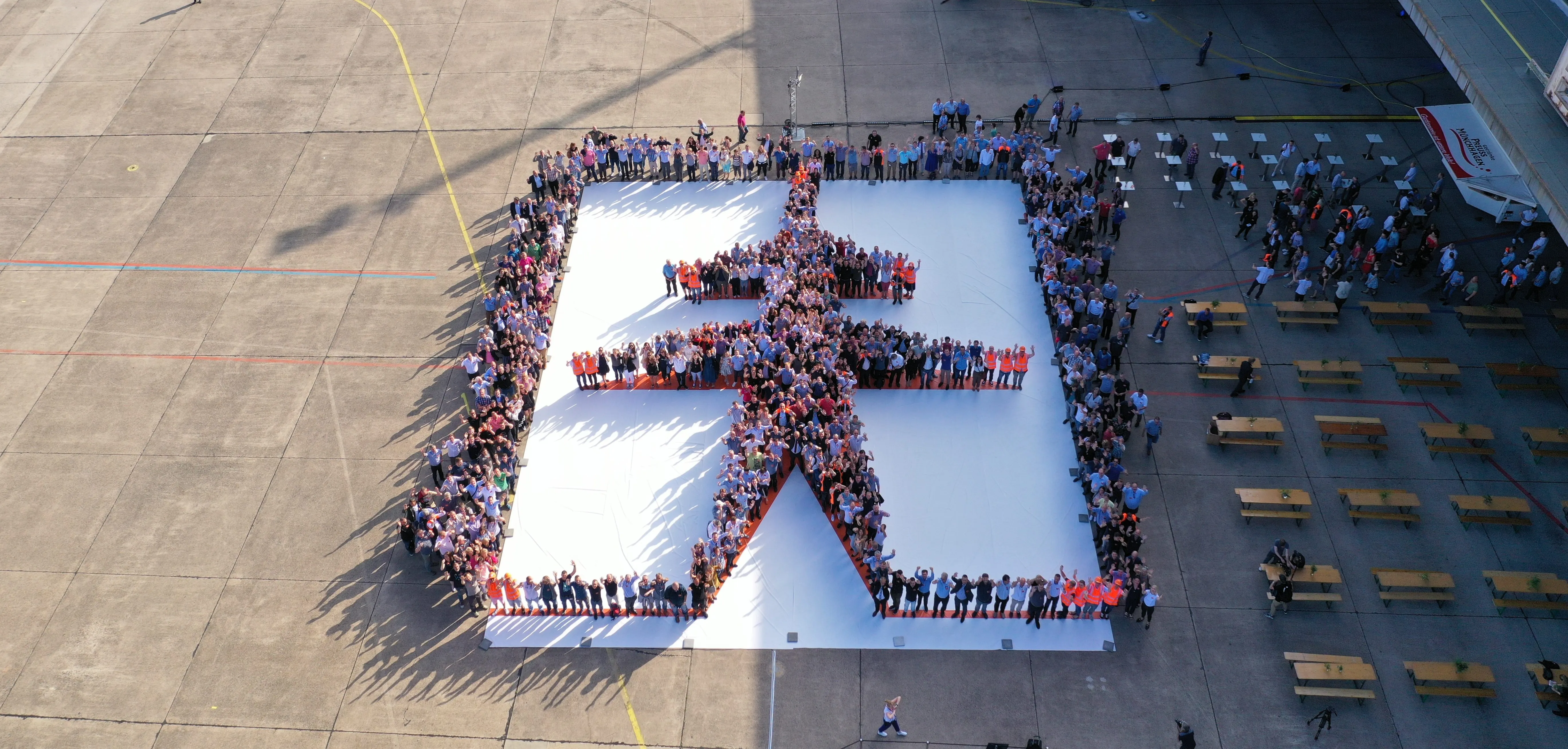 Aerial view of a large group of people forming the 50Hertz logo on a concrete surface, celebrating teamwork and unity.