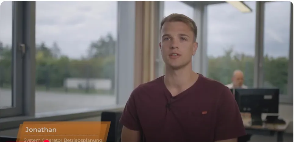 Young professional in a casual shirt discusses system operations at 50Hertz Transmission office.