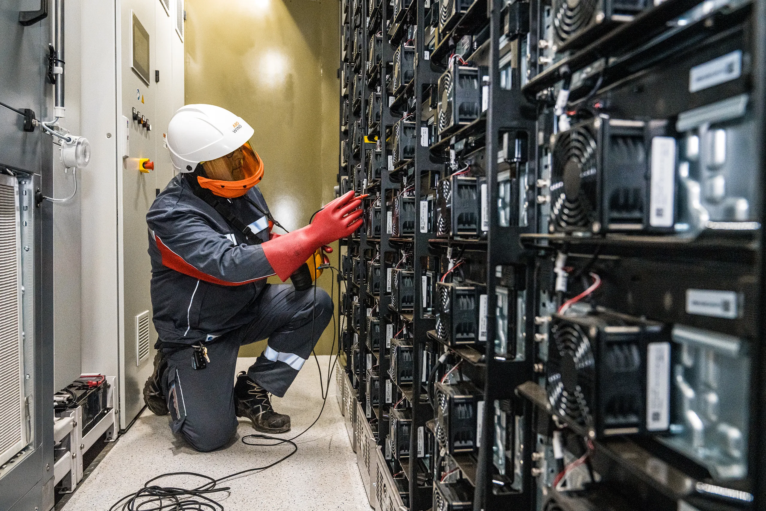 Ein Techniker in Schutzkleidung und Helm arbeitet an einem Batteriesystem in einem Energieversorgungsraum.