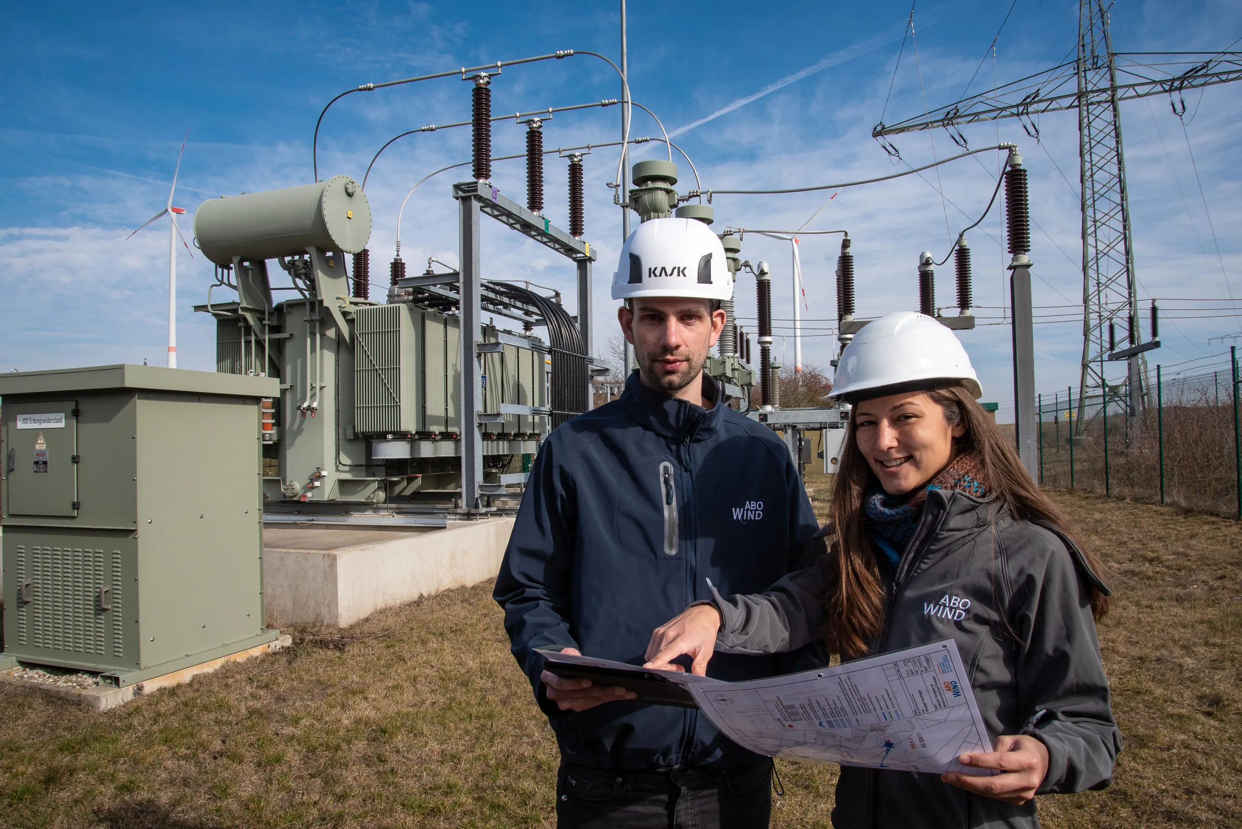 Zwei Ingenieure bei ABO Energy begutachten Pläne vor einer Transformatorstation.
