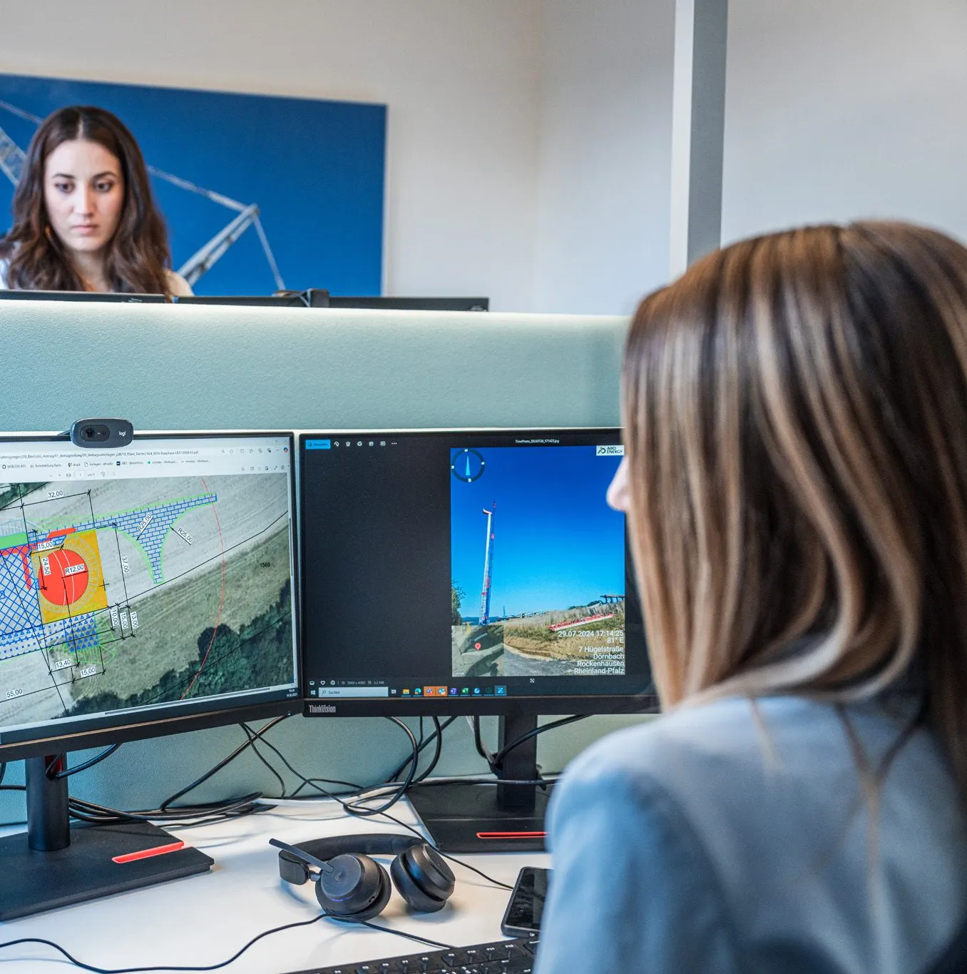 Ein Techniker mit Schutzhelm und Warnweste arbeitet an einem Laptop vor Solarpanels im Freien.