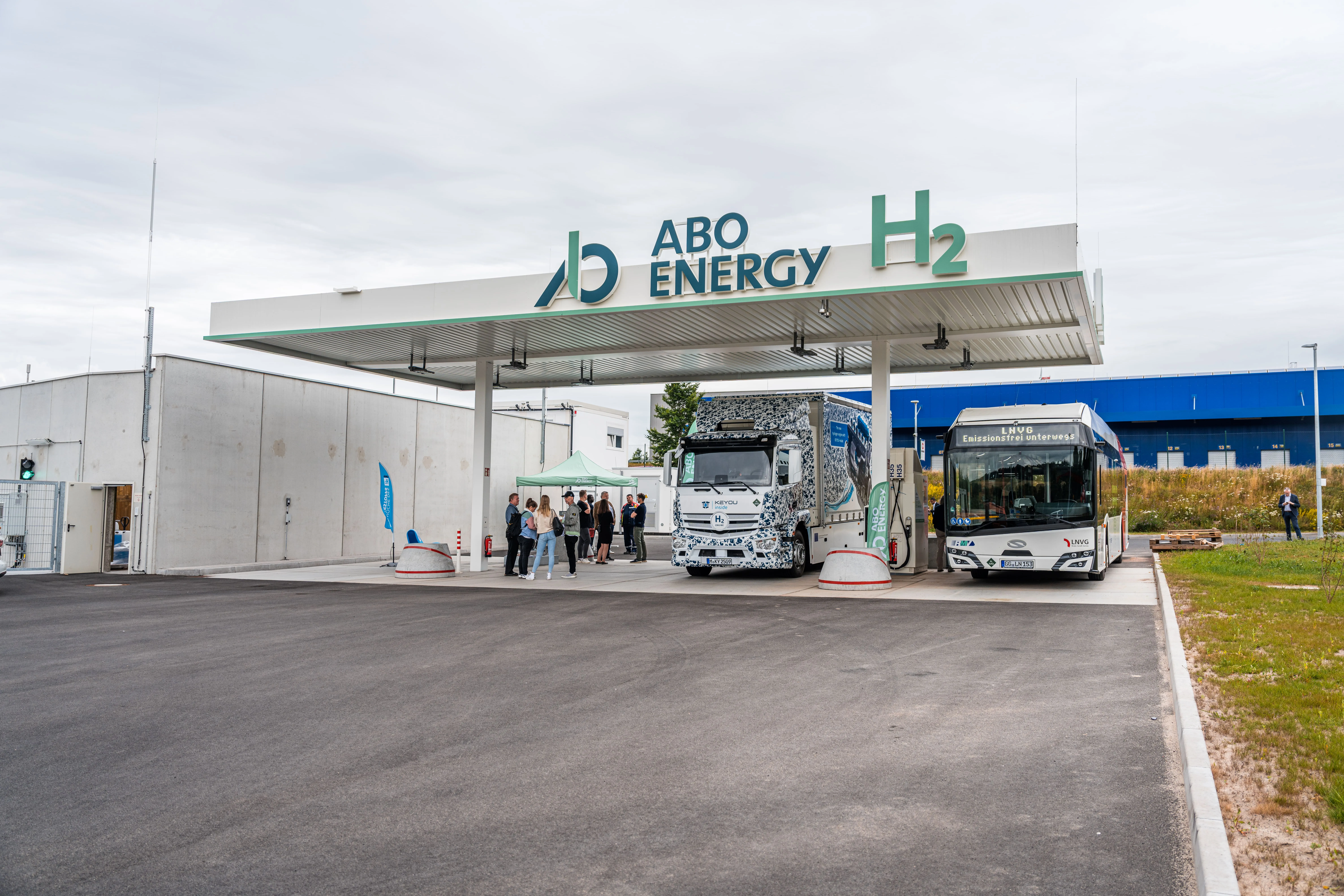 Wasserstofftankstelle von ABO Energy mit LKW und Bus an den Zapfsäulen, Menschen im Hintergrund