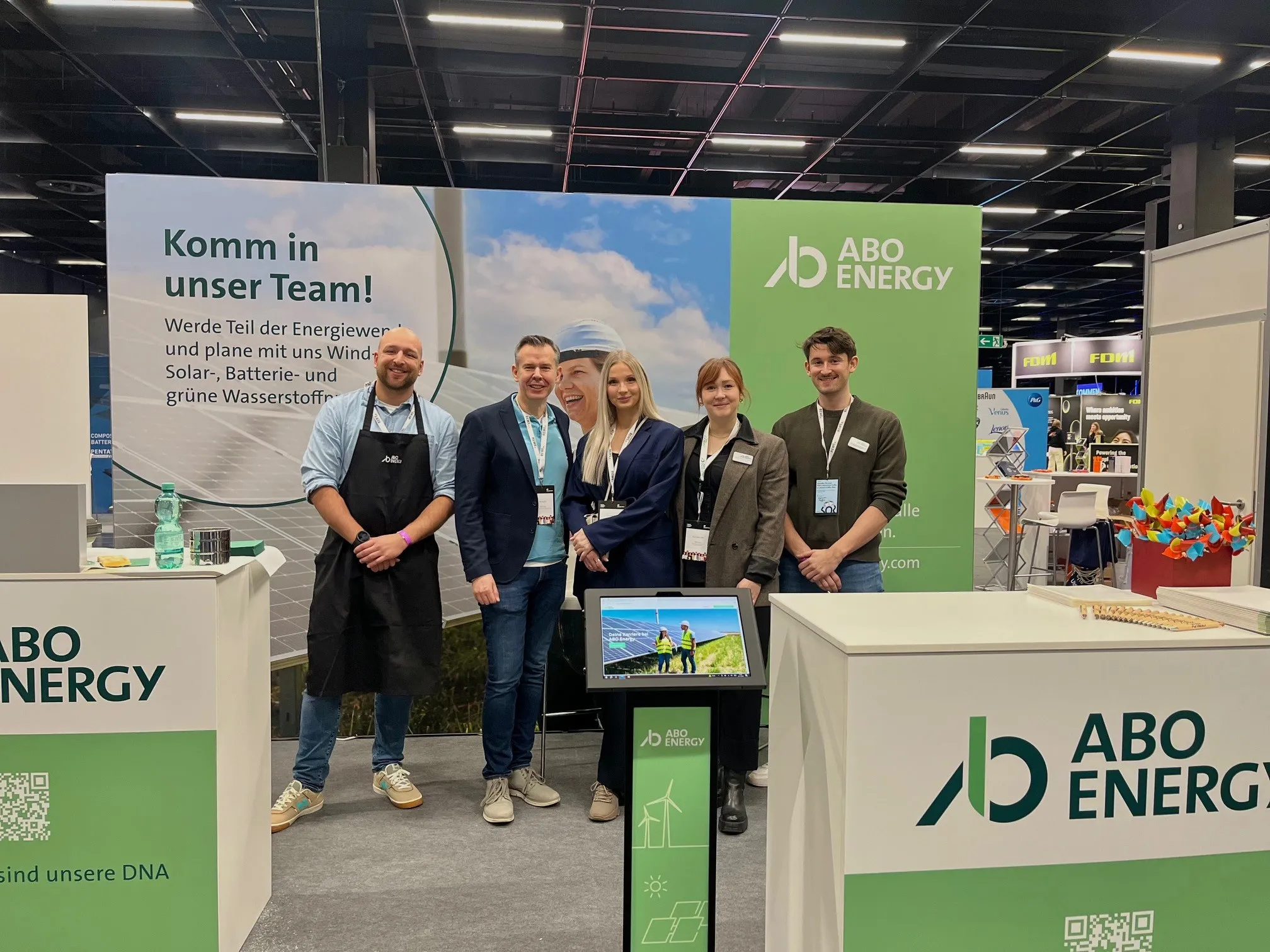 Vier Recruiters stehen vor einem Banner mit der Aufschrift "Komm in unser Team!" auf einer Karrieremesse von ABO Energy.