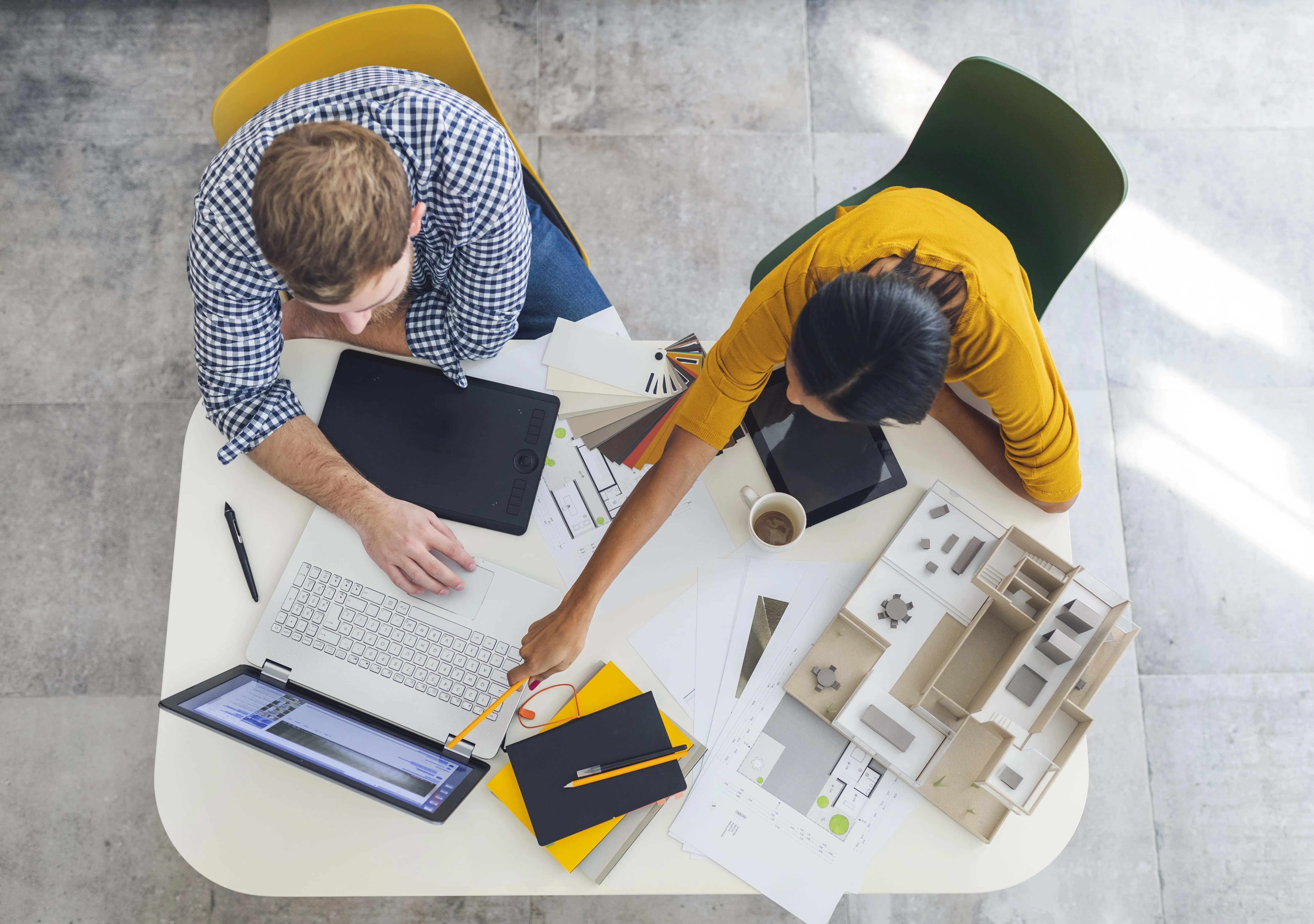 Zwei Berater arbeiten gemeinsam an einem Architekturprojekt mit Laptop, Plänen und Modell auf einem Schreibtisch.