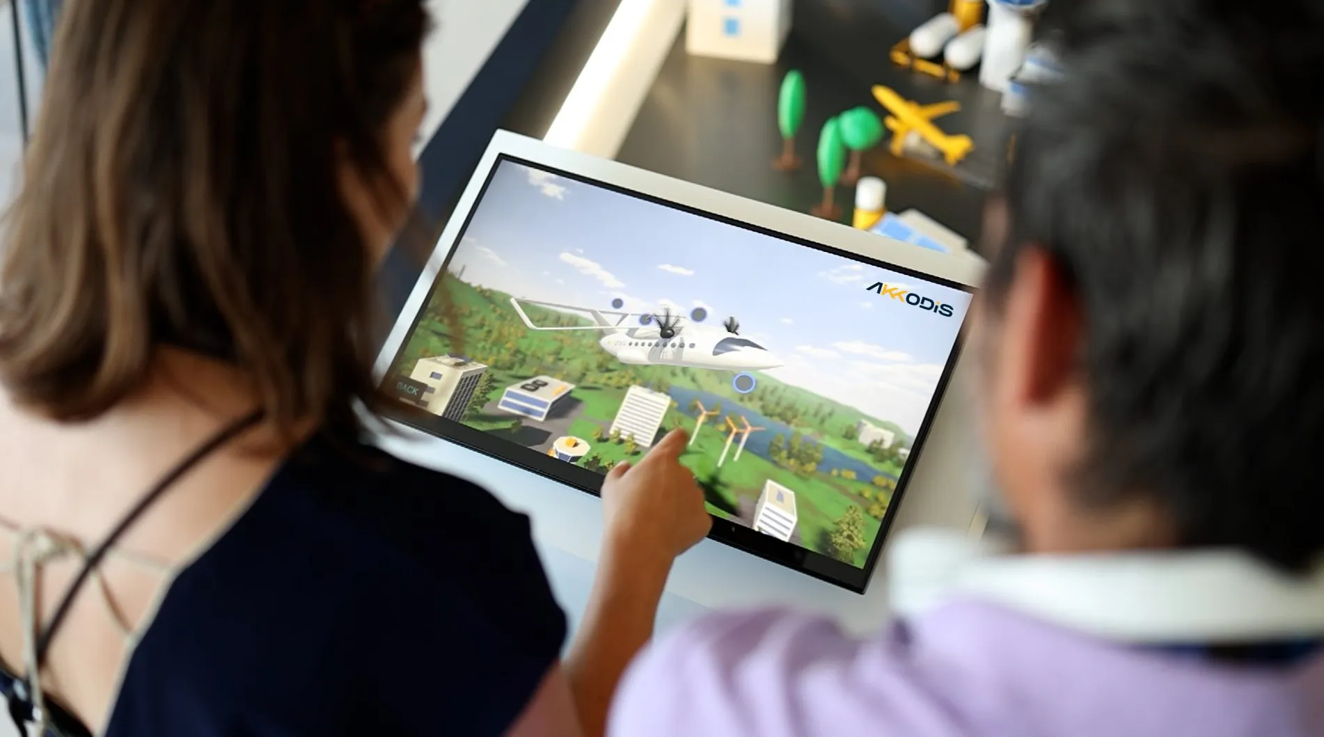 Zwei Personen betrachten auf einem Bildschirm ein digitales Flugzeugmodell mit Akkodis-Logo.