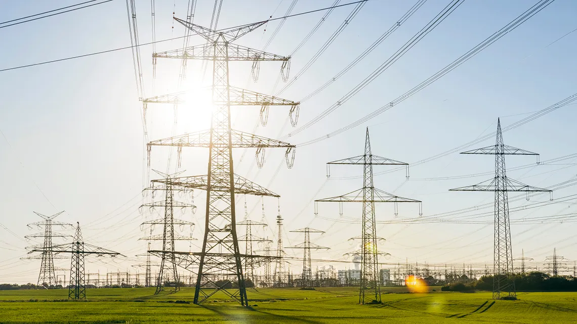 Strommasten auf einem grünen Feld bei Sonnenaufgang, repräsentieren Amprion GmbH im Bereich Energie und Versorgung.