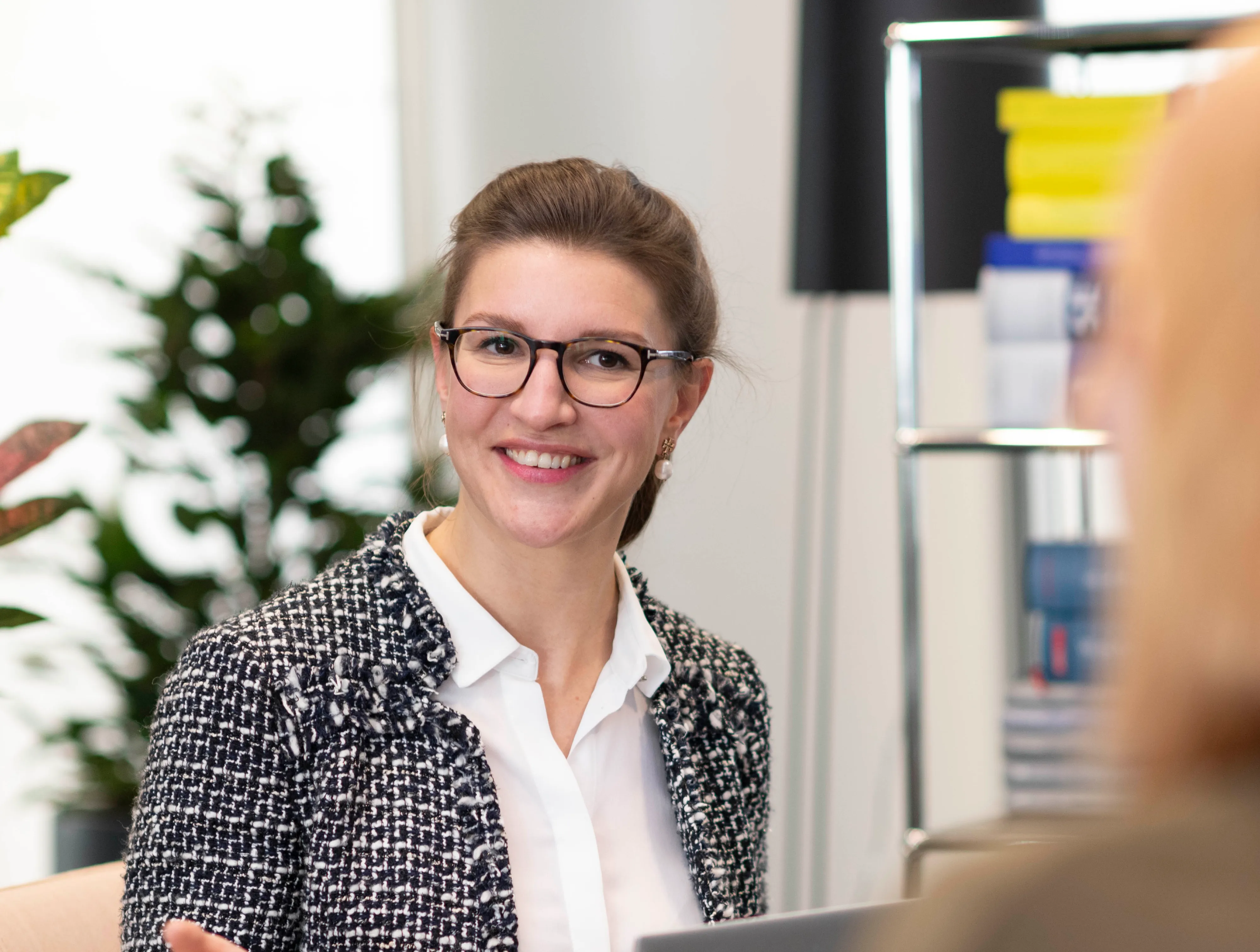 Eine lächelnde Geschäftsfrau im Gespräch mit einer Kollegin in einem modernen Büro bei ARAG SE.