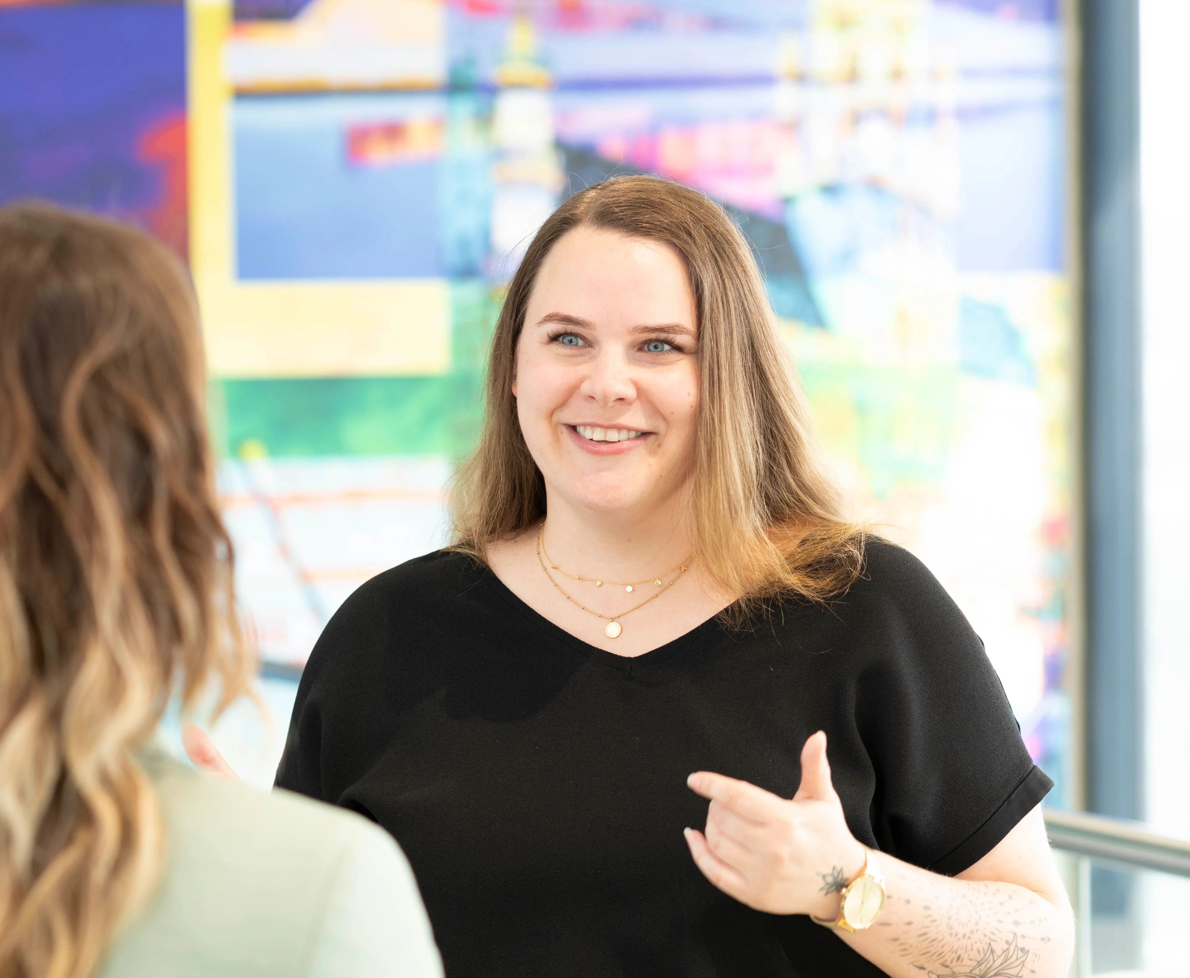 Zwei Personen im Gespräch in einem modernen Büro, eine Frau lächelt und gestikuliert freundlich.