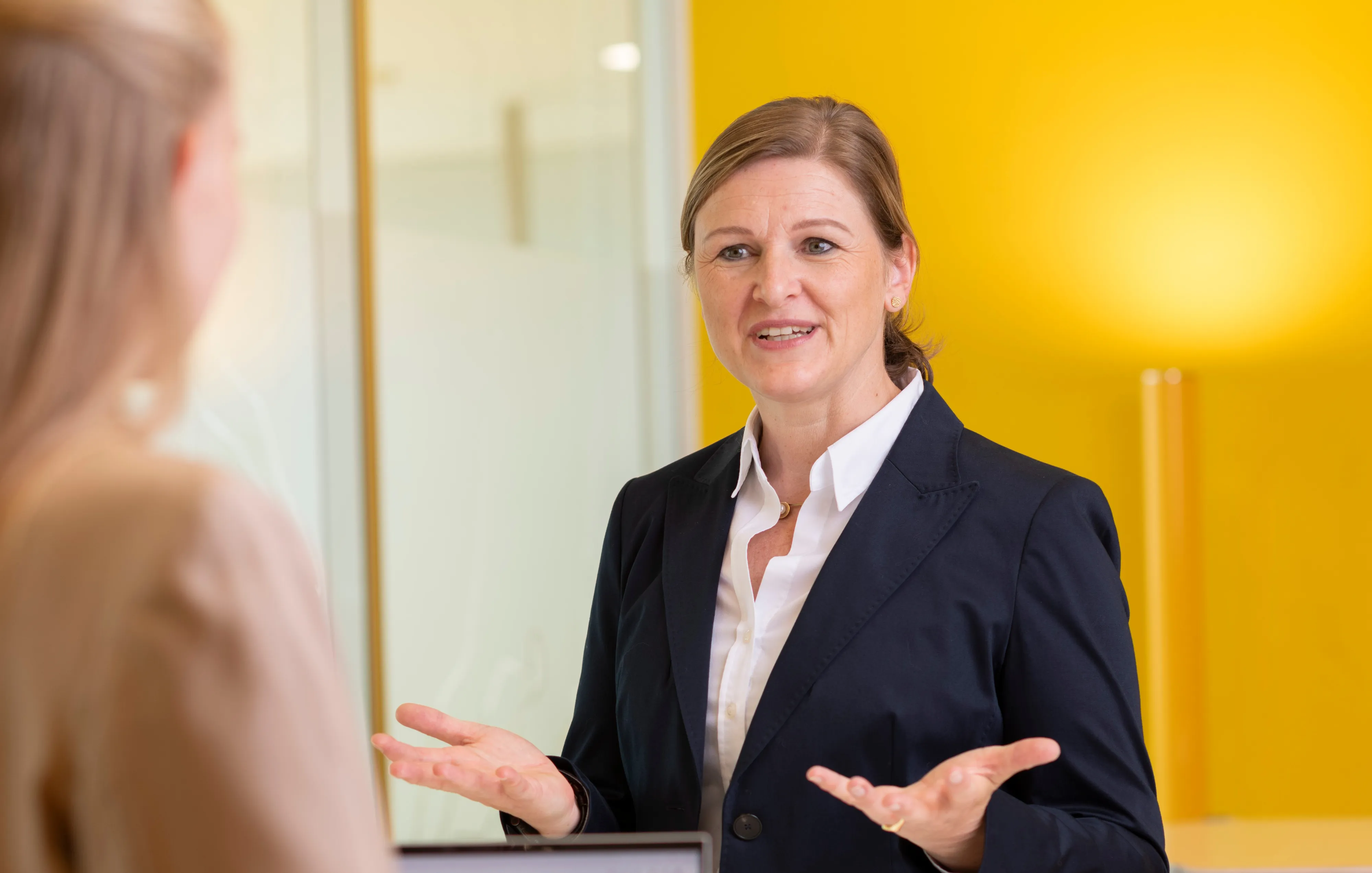 Eine Frau in Business-Kleidung spricht mit einer Kollegin in einem hellen Büro bei ARAG SE.