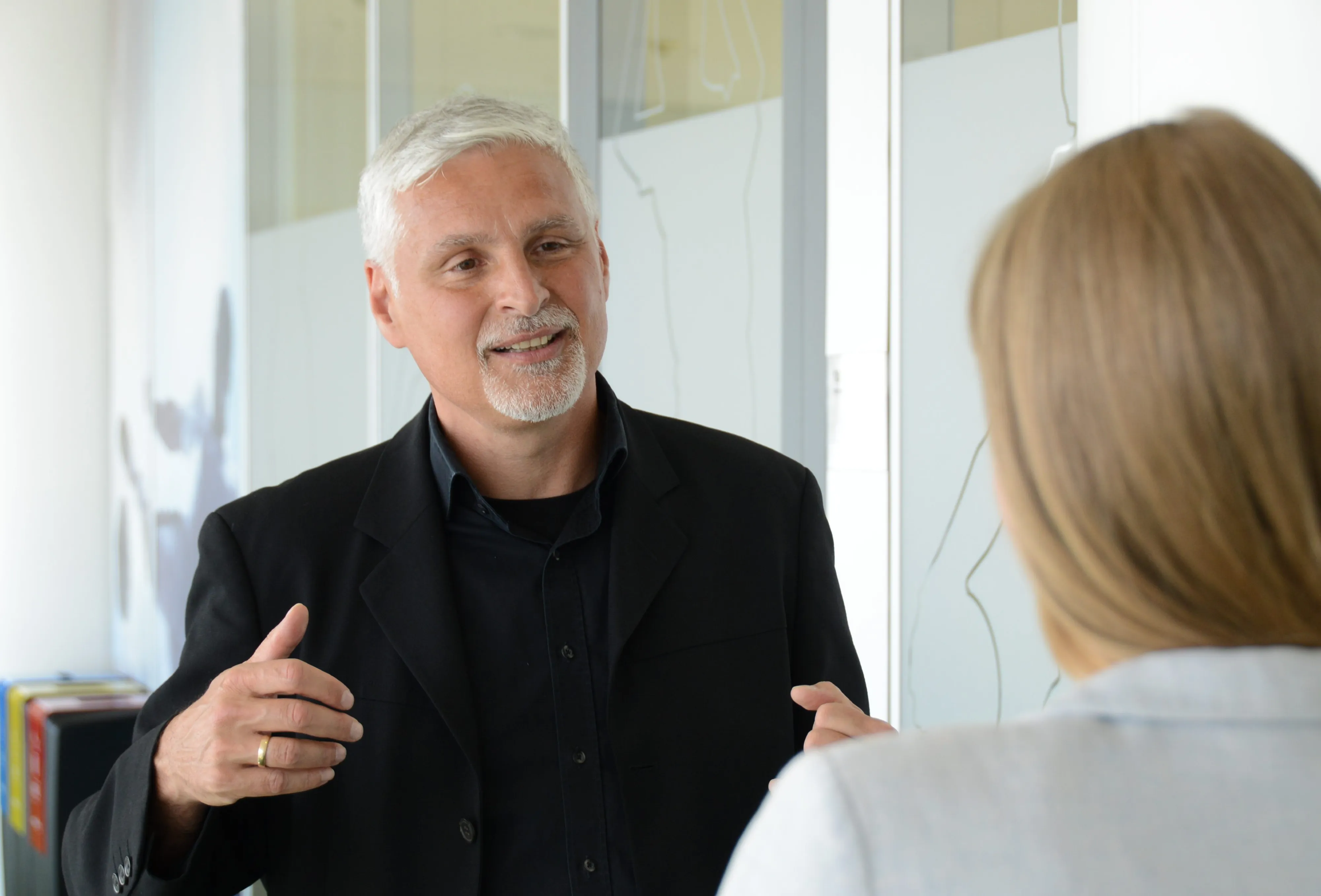 Ein älterer Mann im Anzug spricht lächelnd mit einer Frau in einem modernen Büro bei ARAG SE.