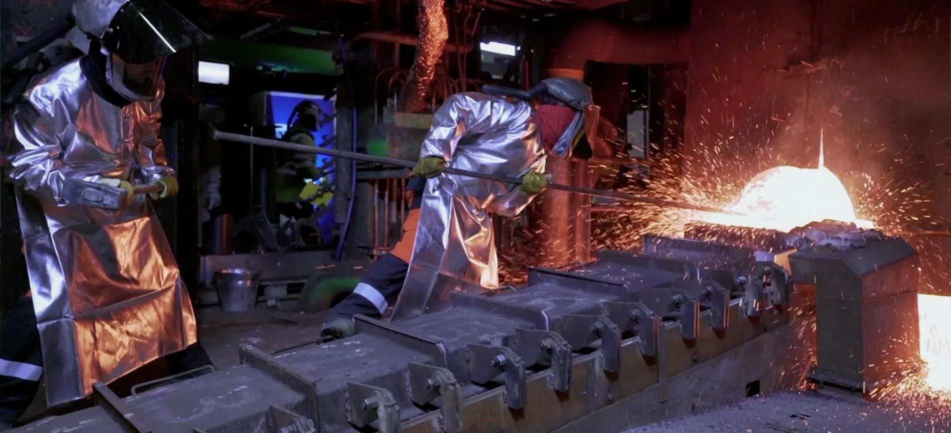 Zwei Mitarbeitende bei Aurubis in Schutzkleidung arbeiten am flüssigen Metall im energieintensiven Schmelzprozess.