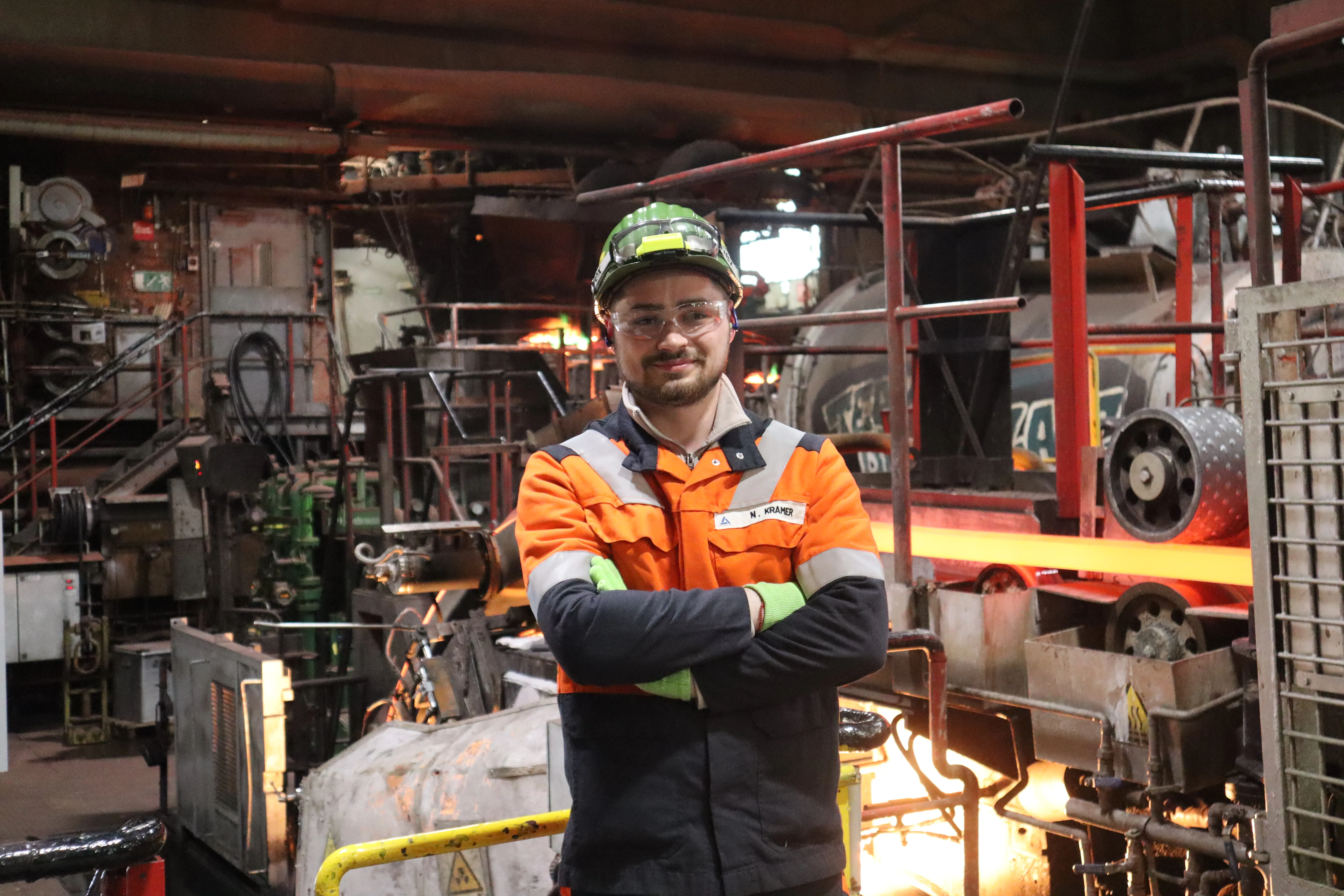 Du siehst einen Mitarbeitenden mit Schutzhelm, der an einem Arbeitstisch Metall mit einem Schweißbrenner bearbeitet.