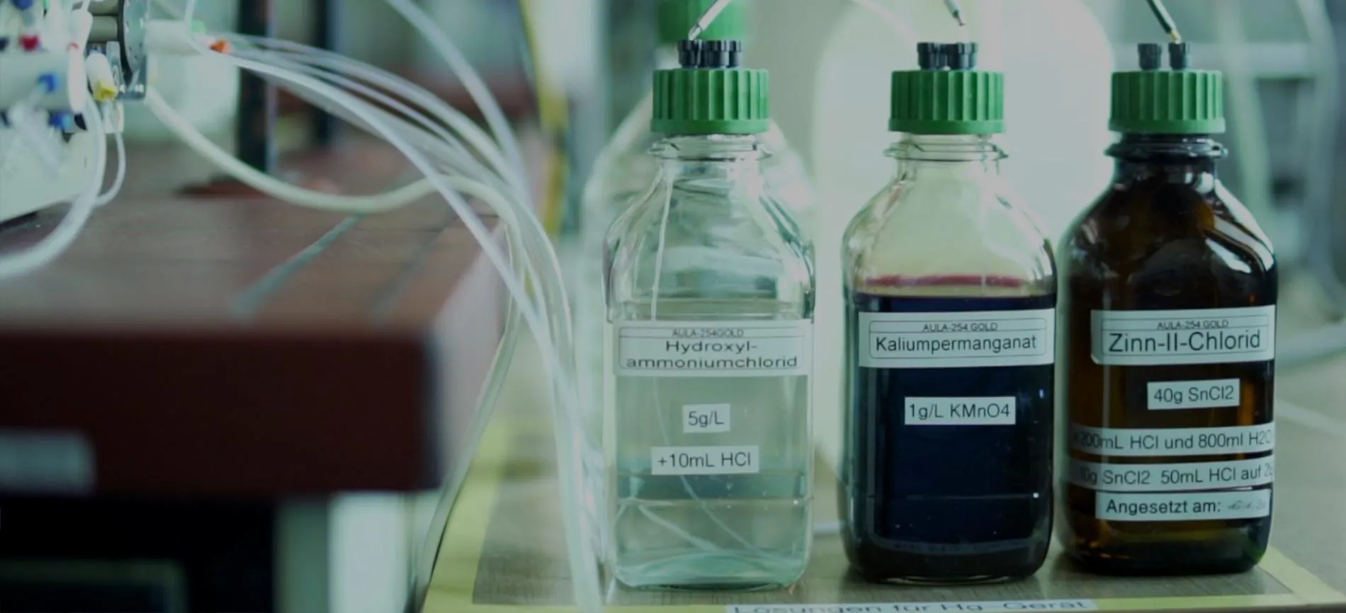Drei Laborflaschen mit Chemikalien und Schläuchen, im Labor von Aurubis für Innovation in Energie und Umwelttechnik.