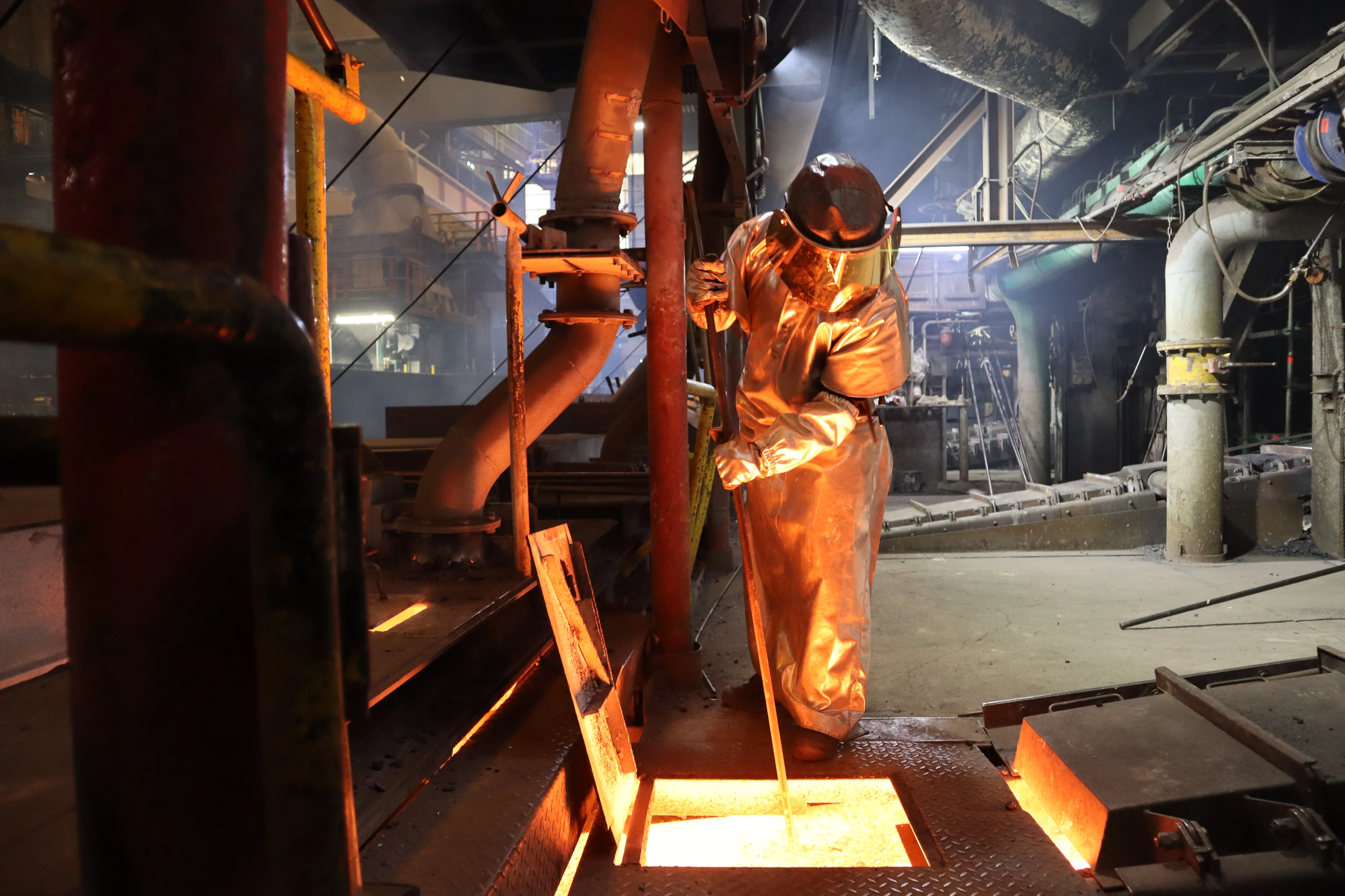 Zwei Mitarbeitende bei Aurubis in Schutzkleidung arbeiten am flüssigen Metall im energieintensiven Schmelzprozess.