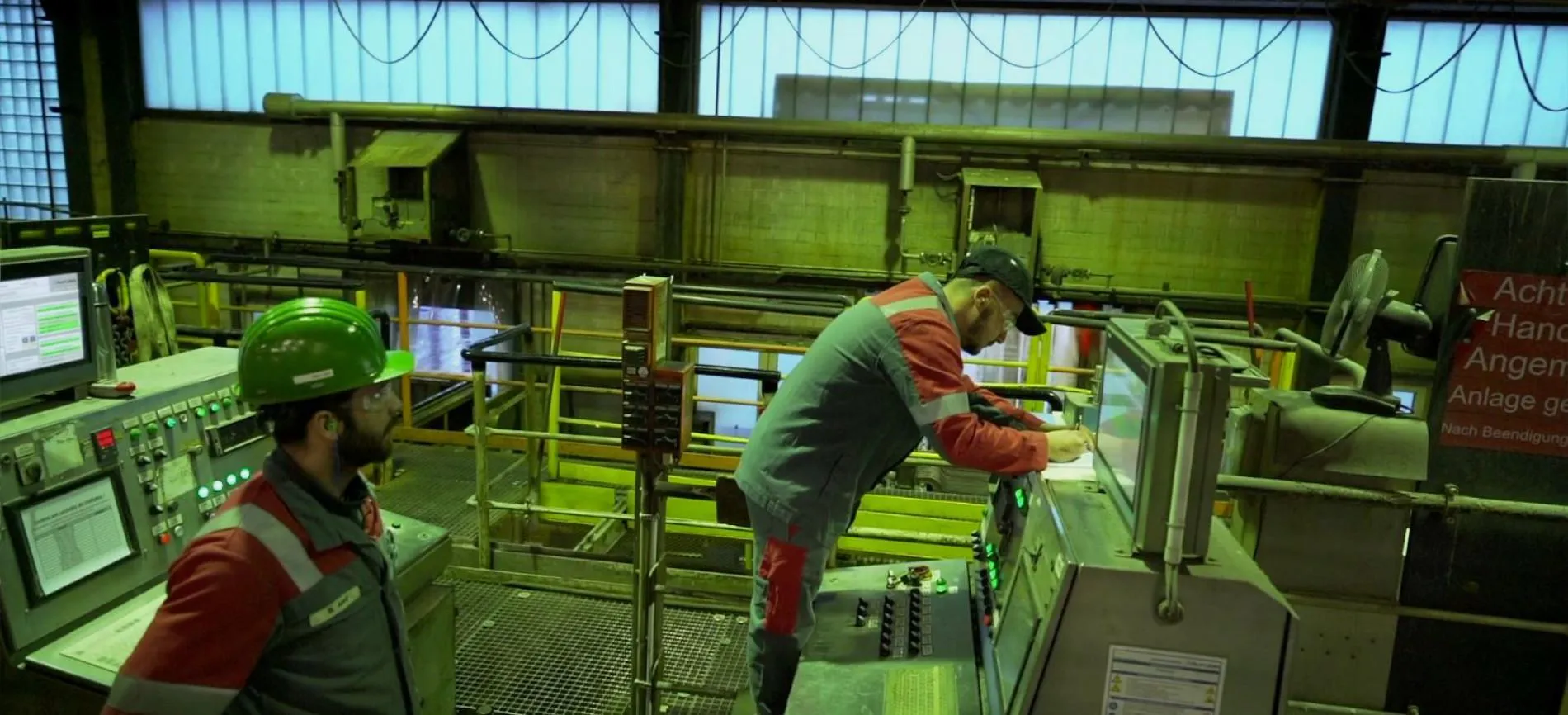 Zwei Mitarbeitende in Schutzkleidung bedienen Steuerpulte in einer modernen Industrieanlage bei Aurubis.