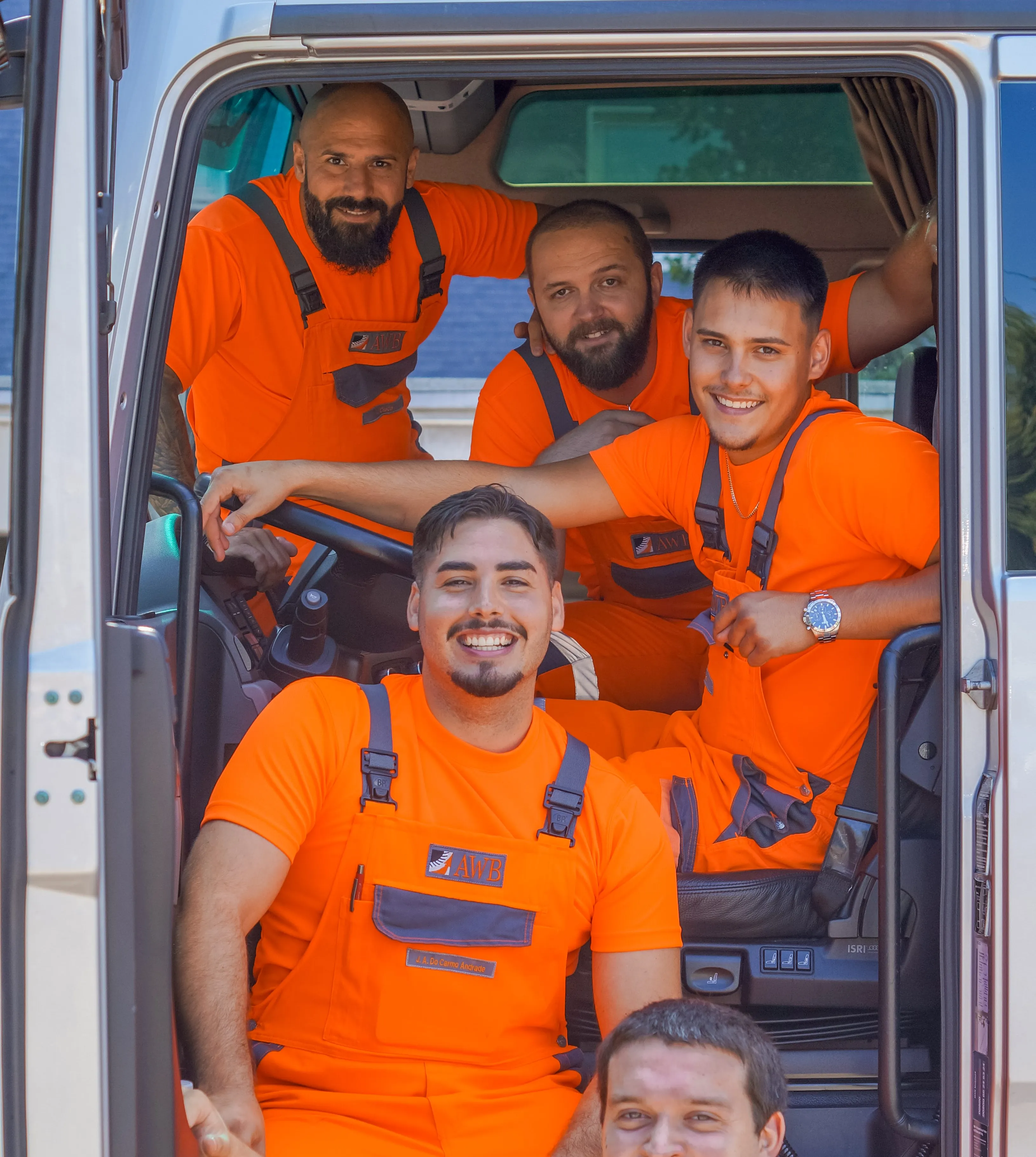 Fünf lächelnde AWB-Mitarbeiter in orangefarbener Arbeitskleidung sitzen gemeinsam im Fahrerhaus eines Müllwagens.