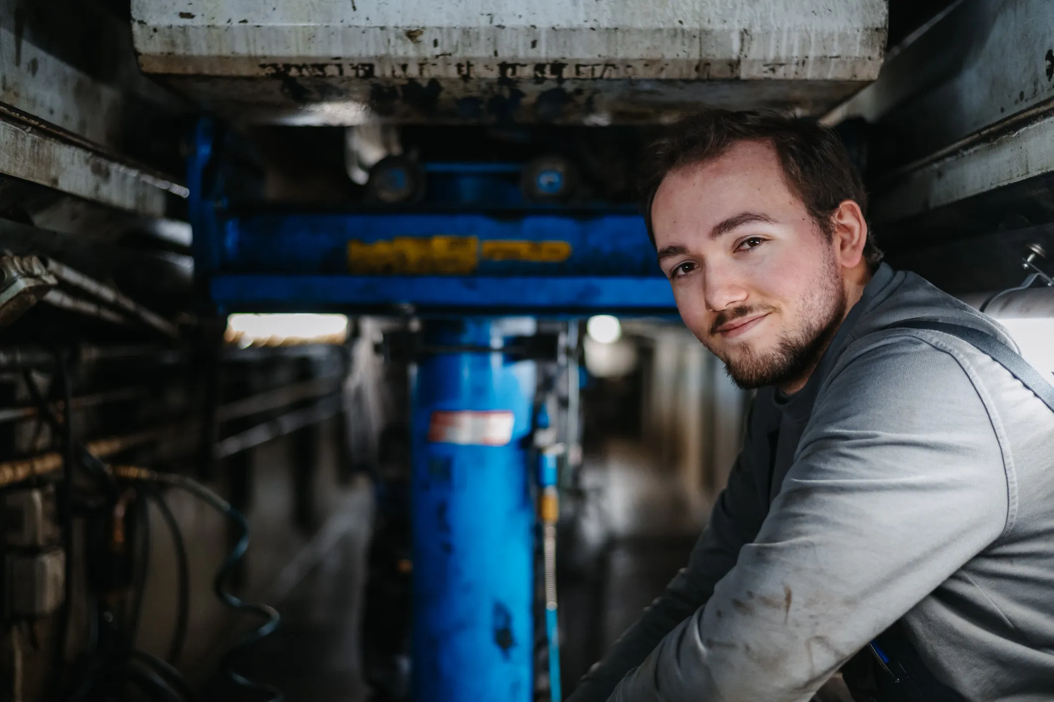 Ein junger Mitarbeiter arbeitet lächelnd an einer Maschine in einer Werkstatt bei AWB Köln.