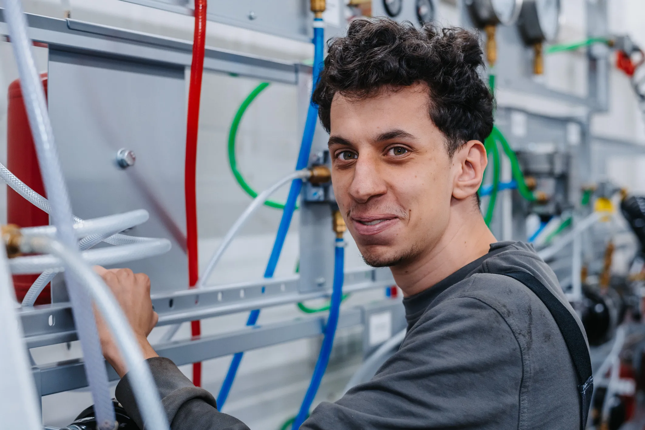 Junger Techniker arbeitet lächelnd an einer Versorgungsanlage bei AWB Köln – werde Teil unseres Teams!
