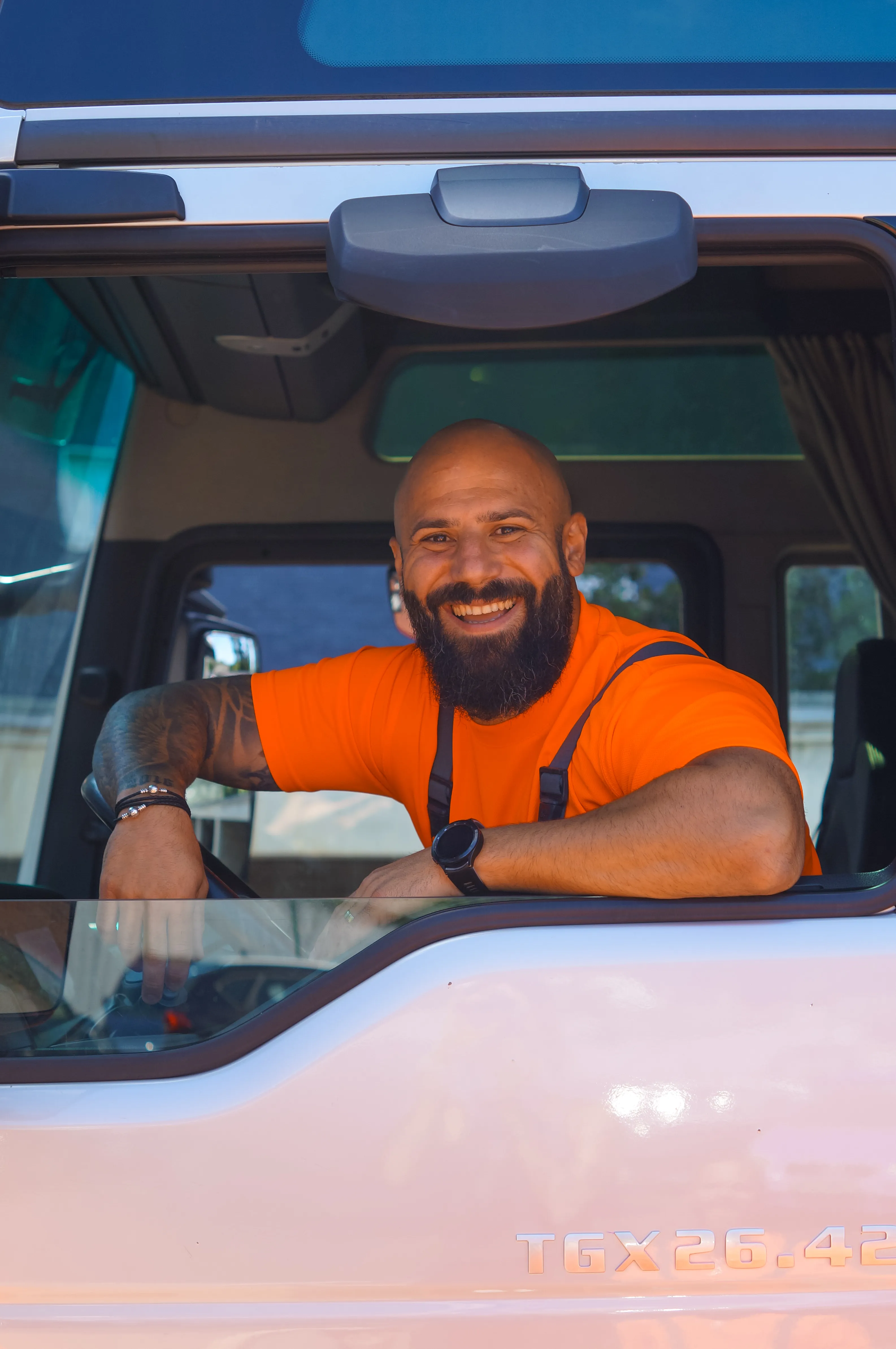 Ein lächelnder AWB-Mitarbeiter im orangefarbenen T-Shirt sitzt am Steuer eines Müllfahrzeugs und schaut aus dem Fenster.