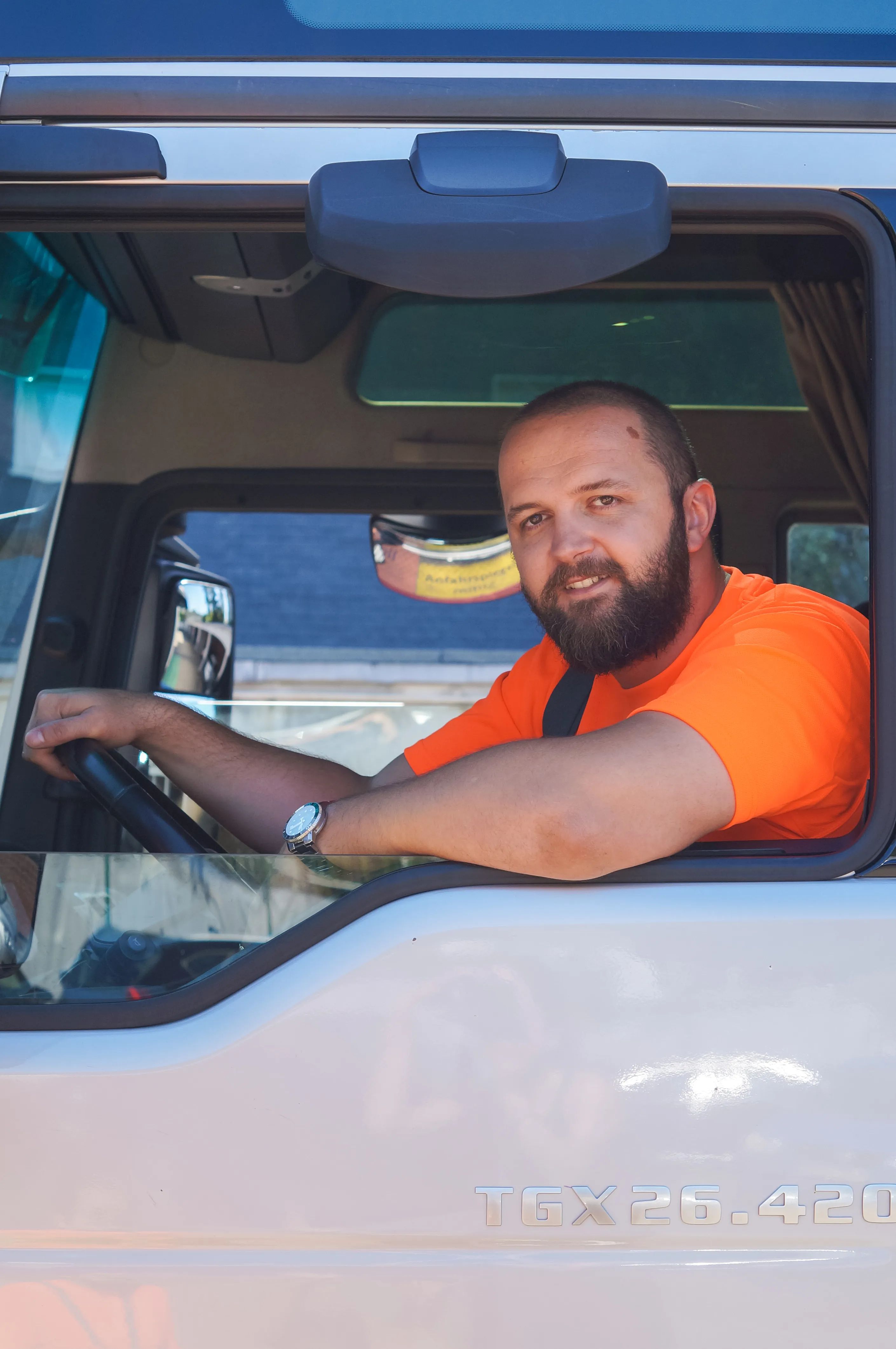 Ein AWB-Mitarbeiter im orangefarbenen Shirt sitzt lächelnd am Steuer eines Müllfahrzeugs und blickt aus dem Fenster.