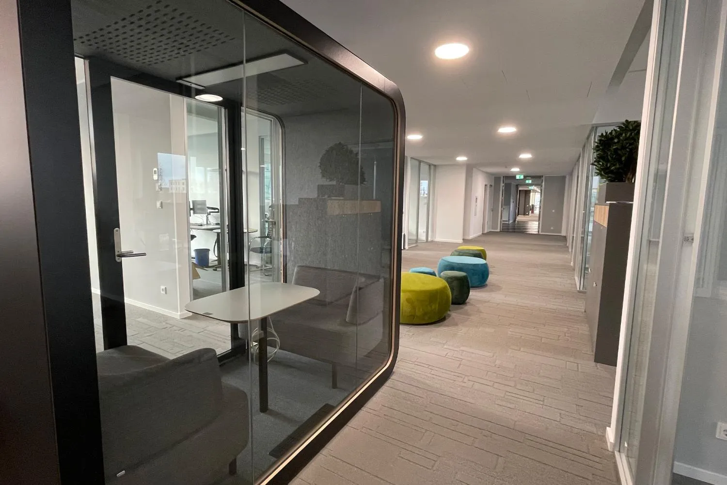 Moderner Flur im BDO-Büro mit Meetingbox und bunten Sitzhockern, der zum Austausch und konzentrierten Arbeiten einlädt.