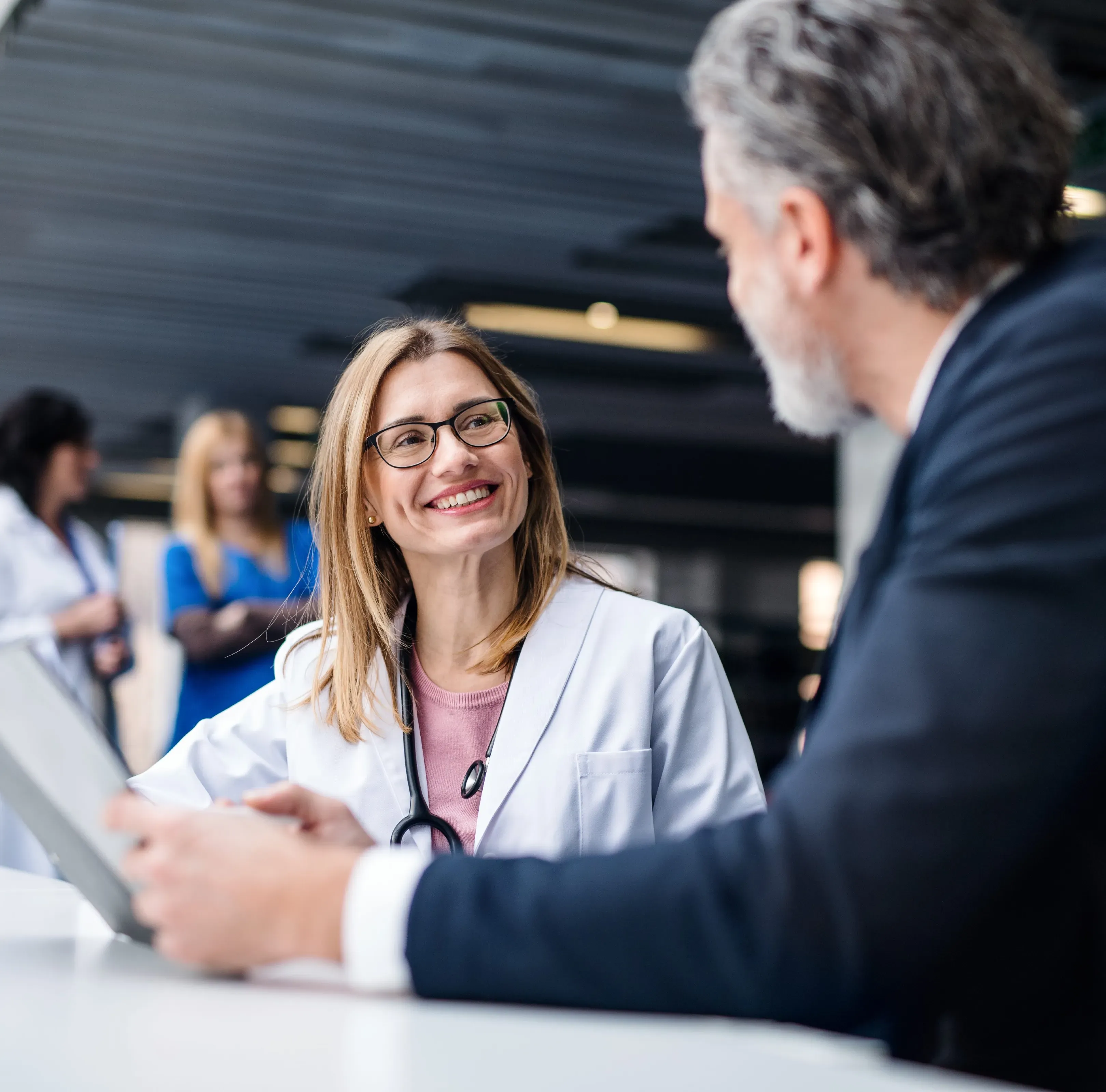 Eine lächelnde Frau im Arztkittel spricht mit einem Kollegen in einem Büro von Berlin-Chemie Menarini.