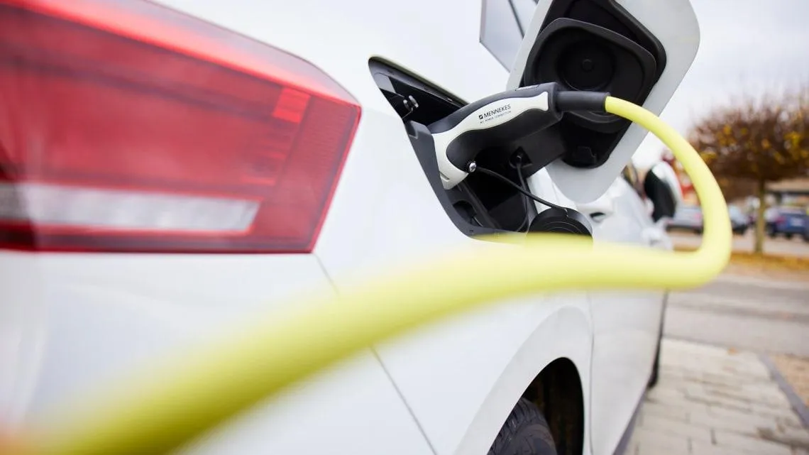 Ein weißes E-Auto wird mit einem Ladekabel an einer Ladesäule geladen – Nachhaltigkeit bei Betty Barclay Group.