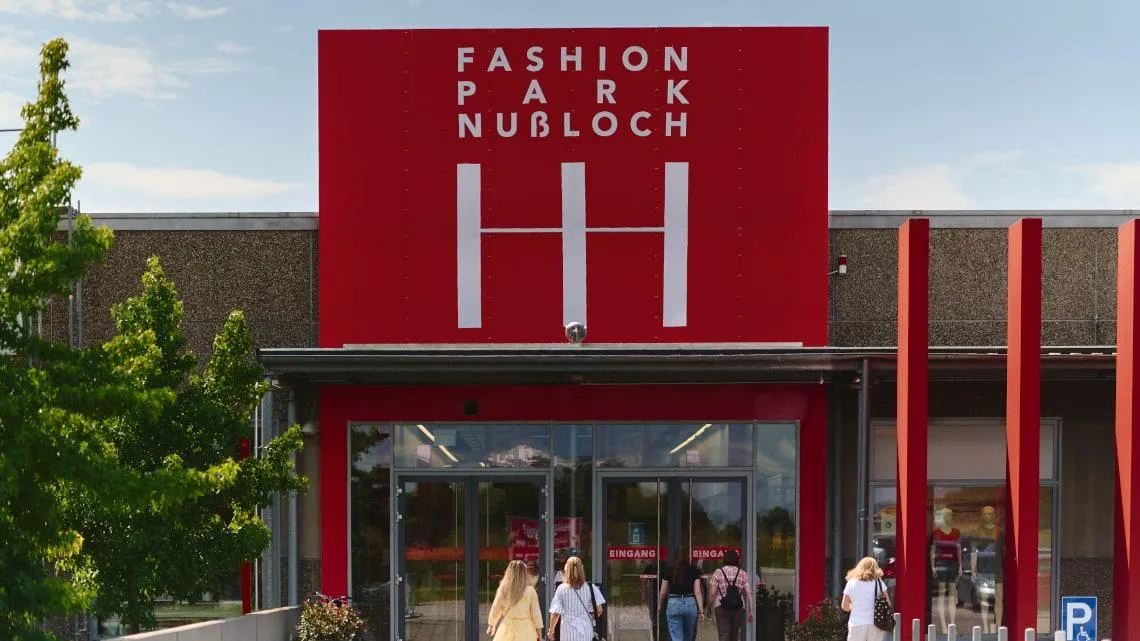 Eingang zum Fashion Park Nussloch mit Menschen, die das Gebäude betreten – entdecke deinen Einstieg im Einzelhandel.