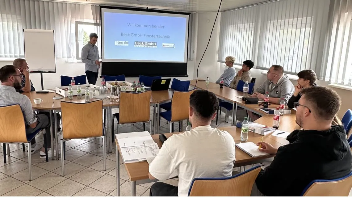 Mehrere junge Erwachsene sitzen in einem Seminarraum und hören bei bewa-plast Beck GmbH Fenstertechnik einer Präsentation zu.