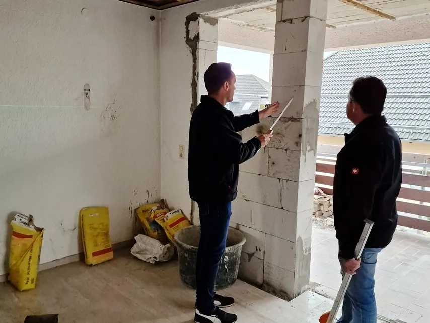 Zwei Kollegen messen gemeinsam eine Fensteröffnung auf einer Baustelle, um den Einbau vorzubereiten.