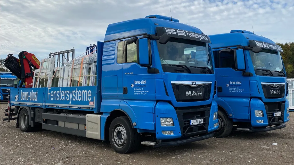 Zwei blaue LKWs von bewa-plast transportieren Fenstersysteme auf dem Firmengelände.