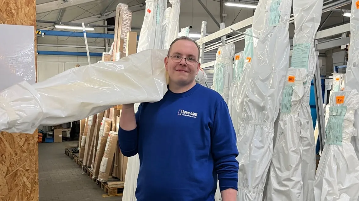 Mitarbeiter trägt verpacktes Fensterprofil auf der Schulter in der Produktion bei bewa-plast Beck GmbH.