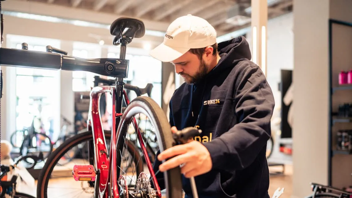 Du siehst einen Mitarbeiter von BIKE24, der ein Fahrrad in der Werkstatt sorgfältig wartet und repariert.