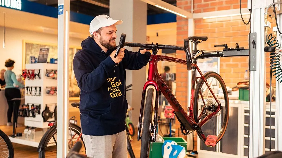 Ein Mitarbeiter von Bike24 prüft ein Fahrrad in der Werkstatt, umgeben von modernem Ladenambiente.