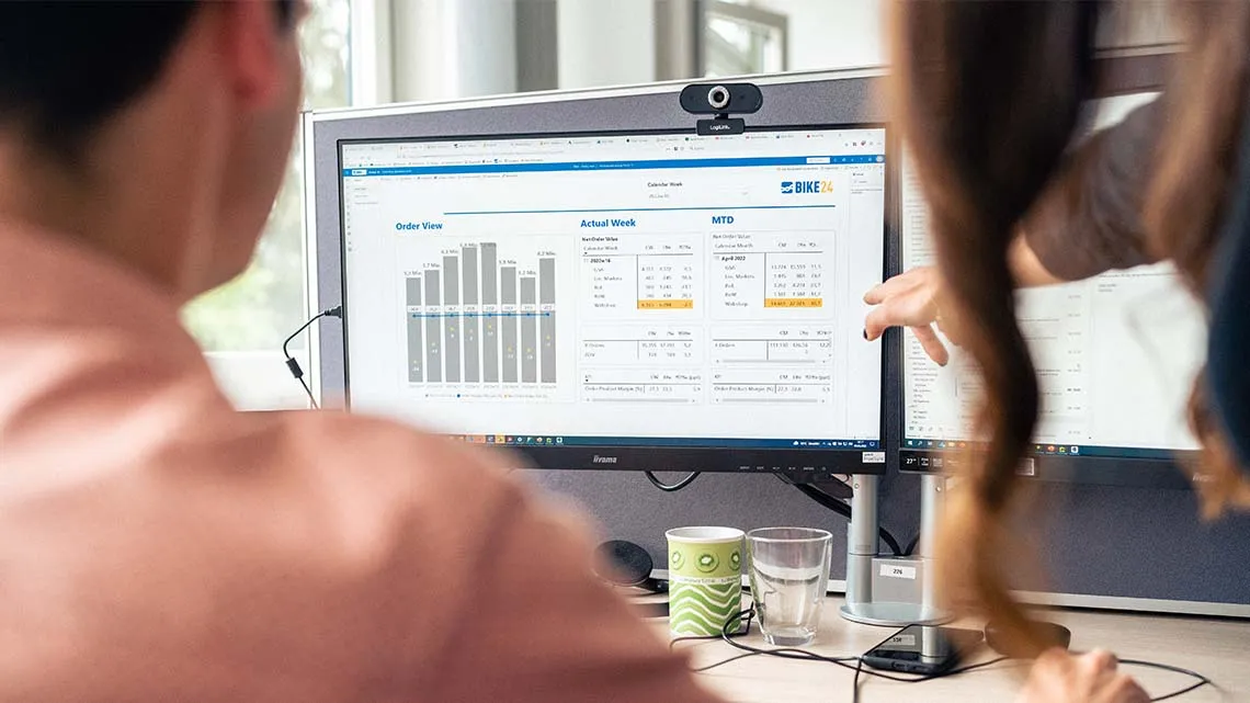 Zwei Mitarbeitende bei BIKE24 analysieren Verkaufszahlen am Bildschirm im modernen Büro.