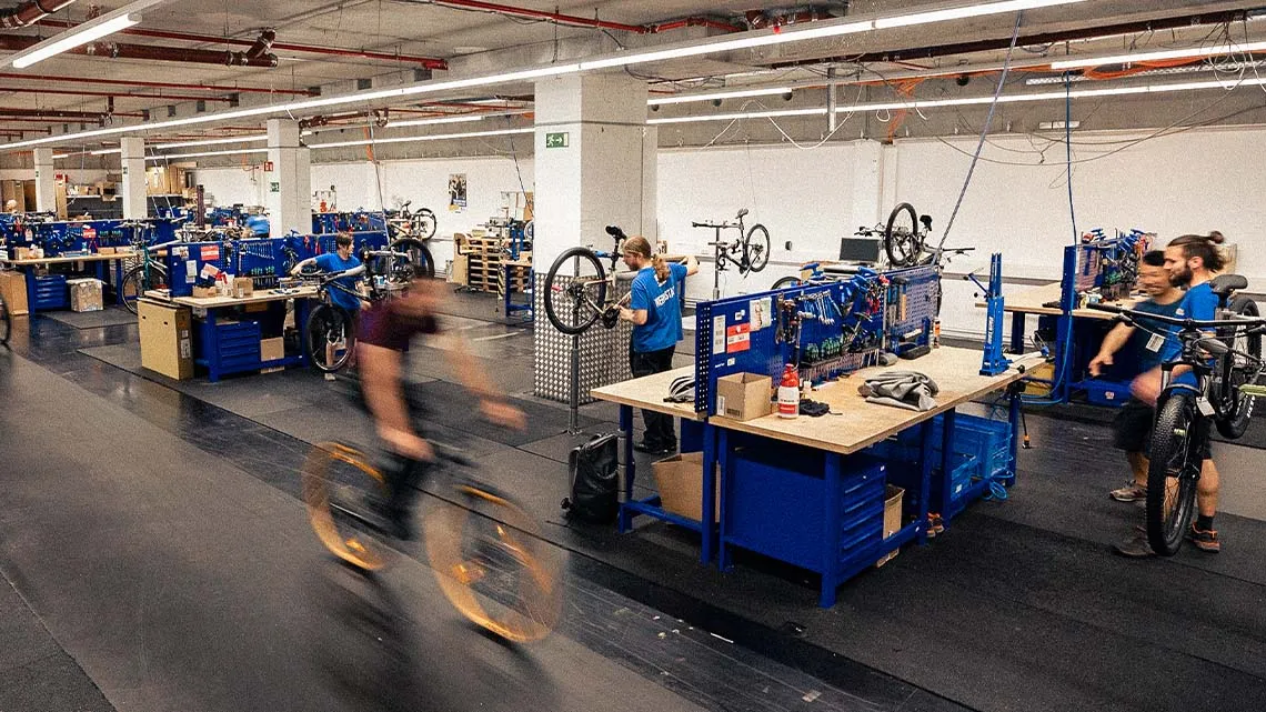 Mehrere Mitarbeitende bauen und reparieren Fahrräder in einer modernen Werkstatt bei BIKE24.