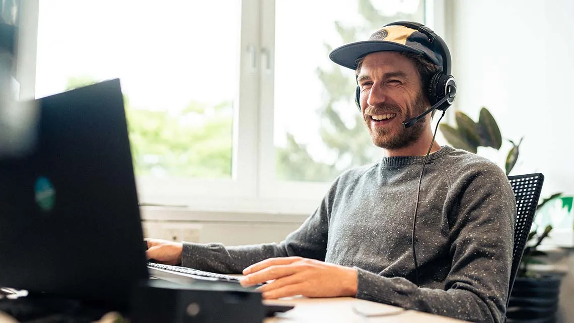 Junger Mann mit Headset arbeitet lächelnd am Laptop im modernen Büro von Bike24 GmbH.