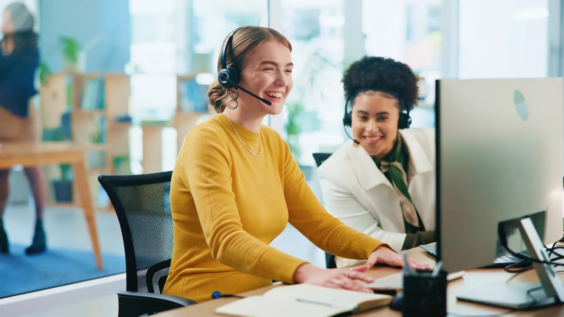 Zwei freundliche Mitarbeiterinnen mit Headsets unterstützen Dich im modernen Büro der BKK Linde im Gesundheitswesen.(iStock / Jacob Wackerhausen)