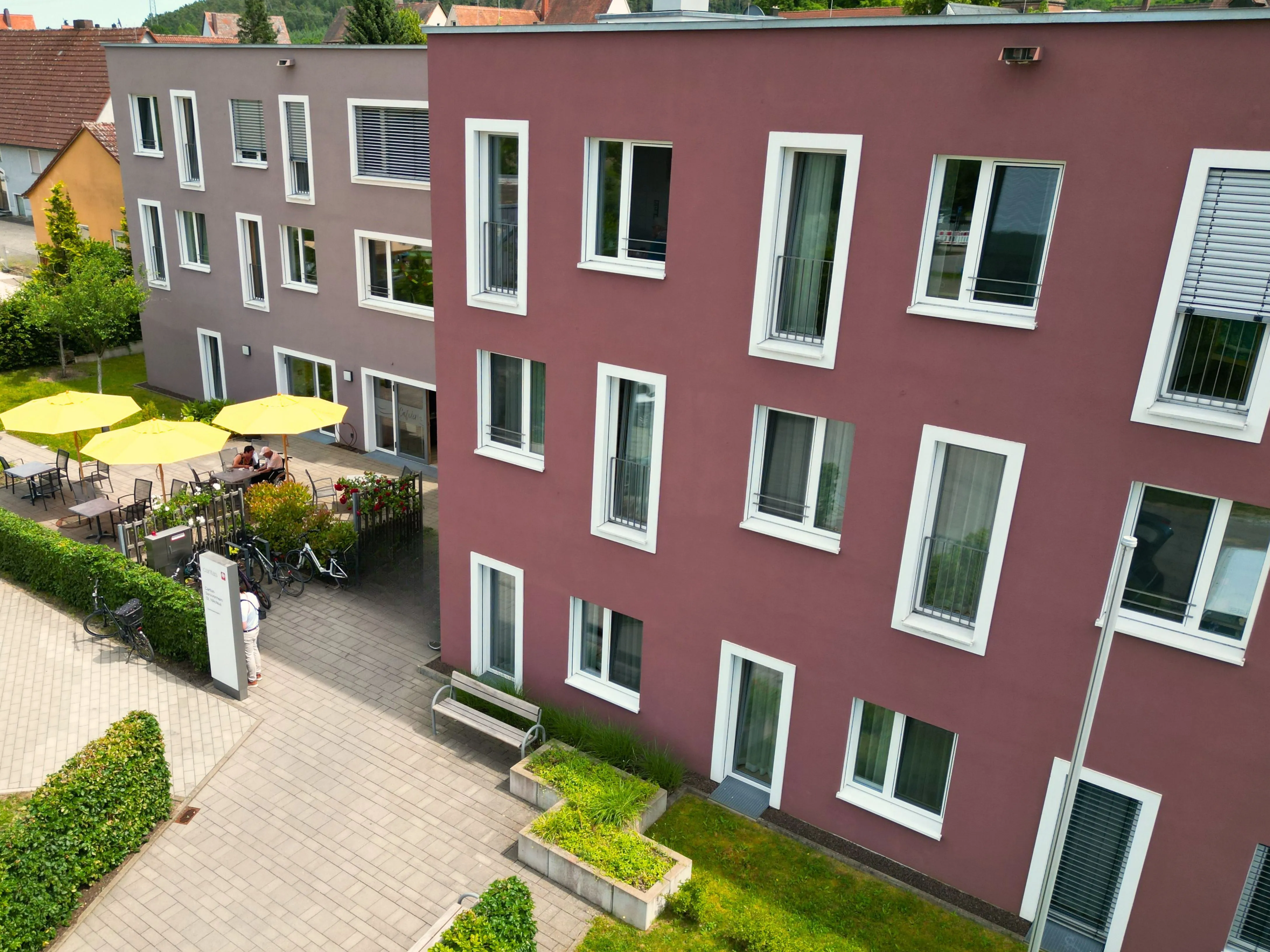 Ein modernes Gebäude von Caritas Mittelbayern mit einem sonnigen Innenhof und gelben Sonnenschirmen.