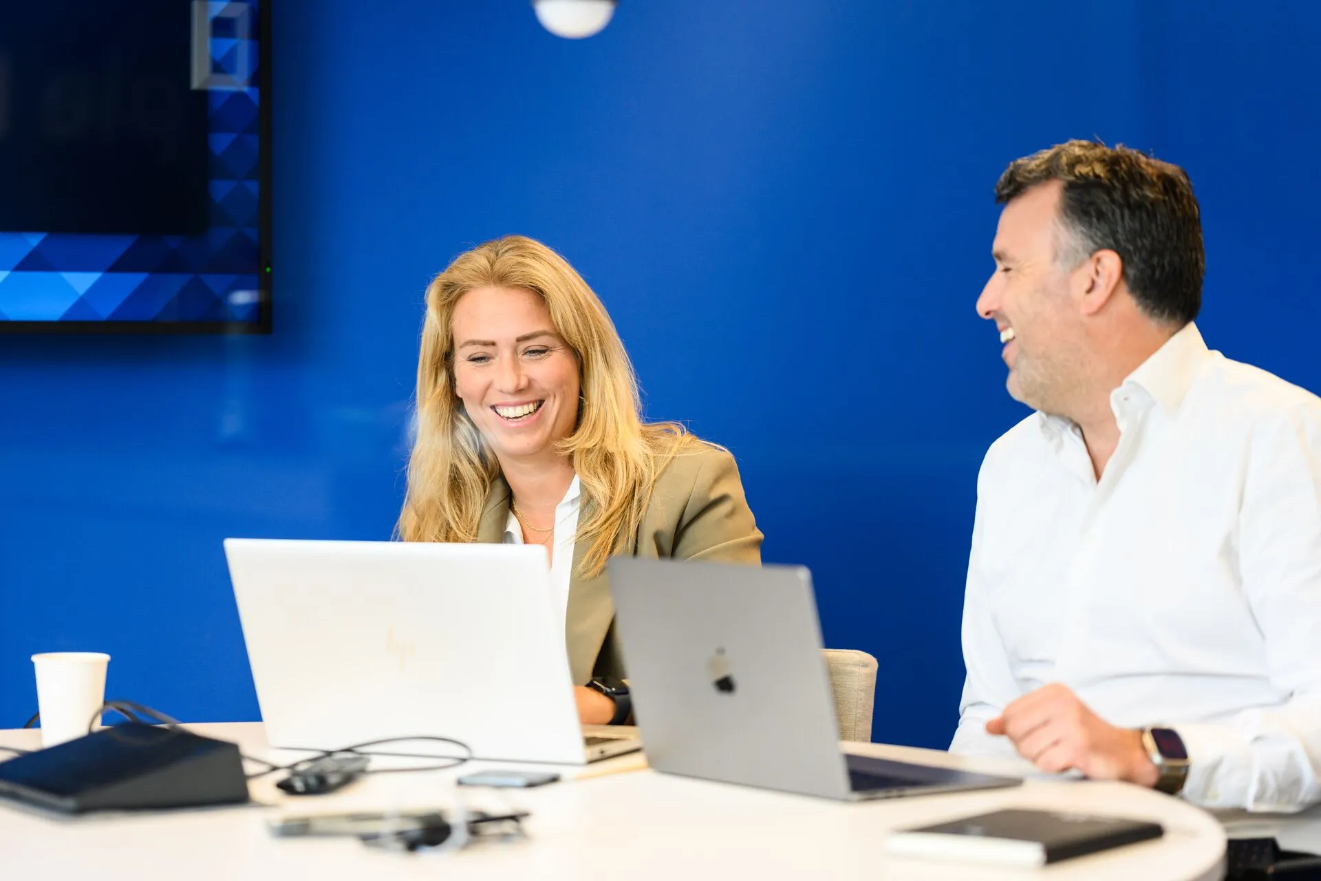 Zwei Kollegen im IT-Bereich arbeiten gemeinsam lachend an Laptops in einem modernen Büro bei Computacenter..