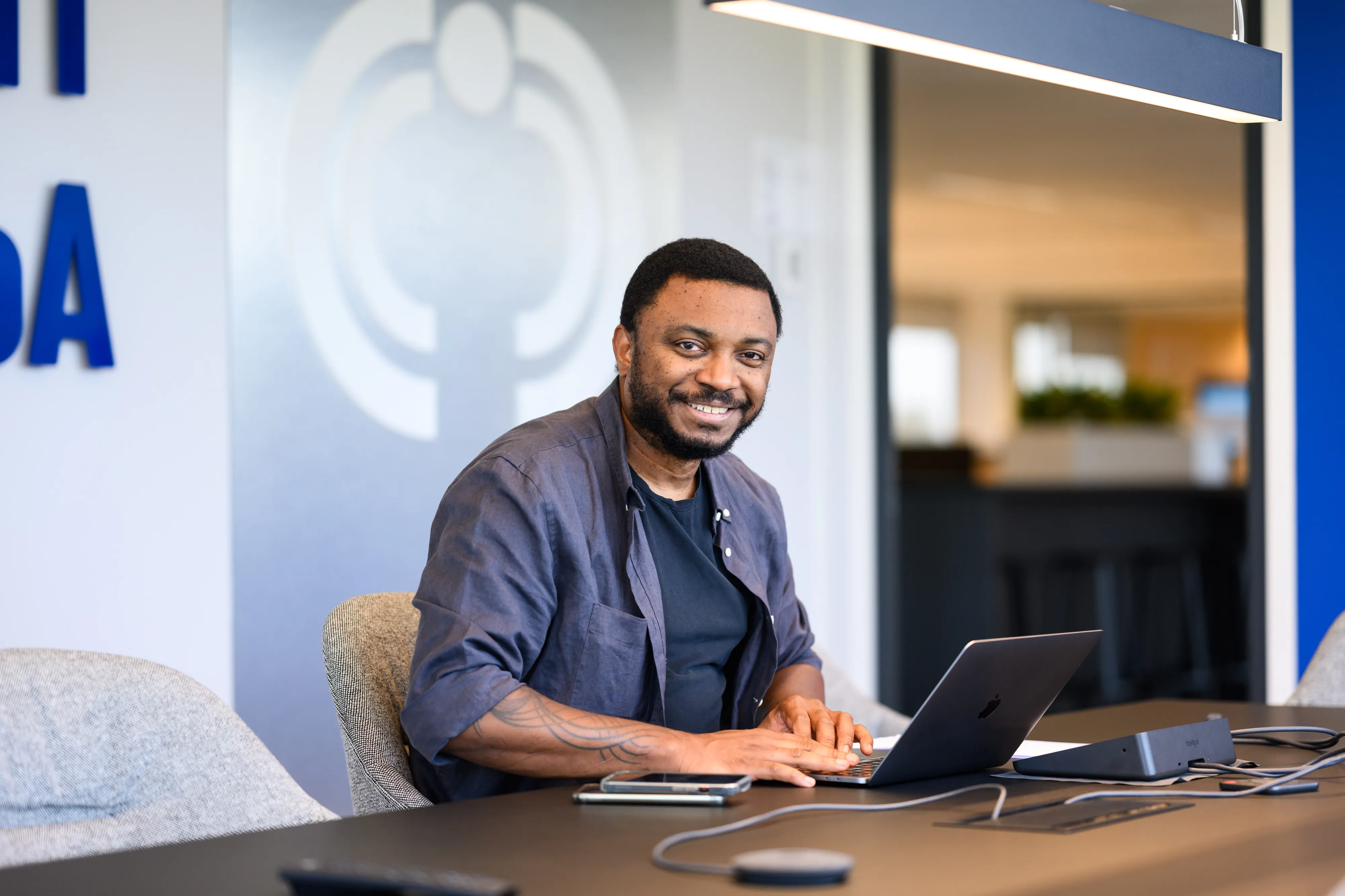 Smiling professional in a bright pink blazer working on a laptop in a modern, tech-savvy office.