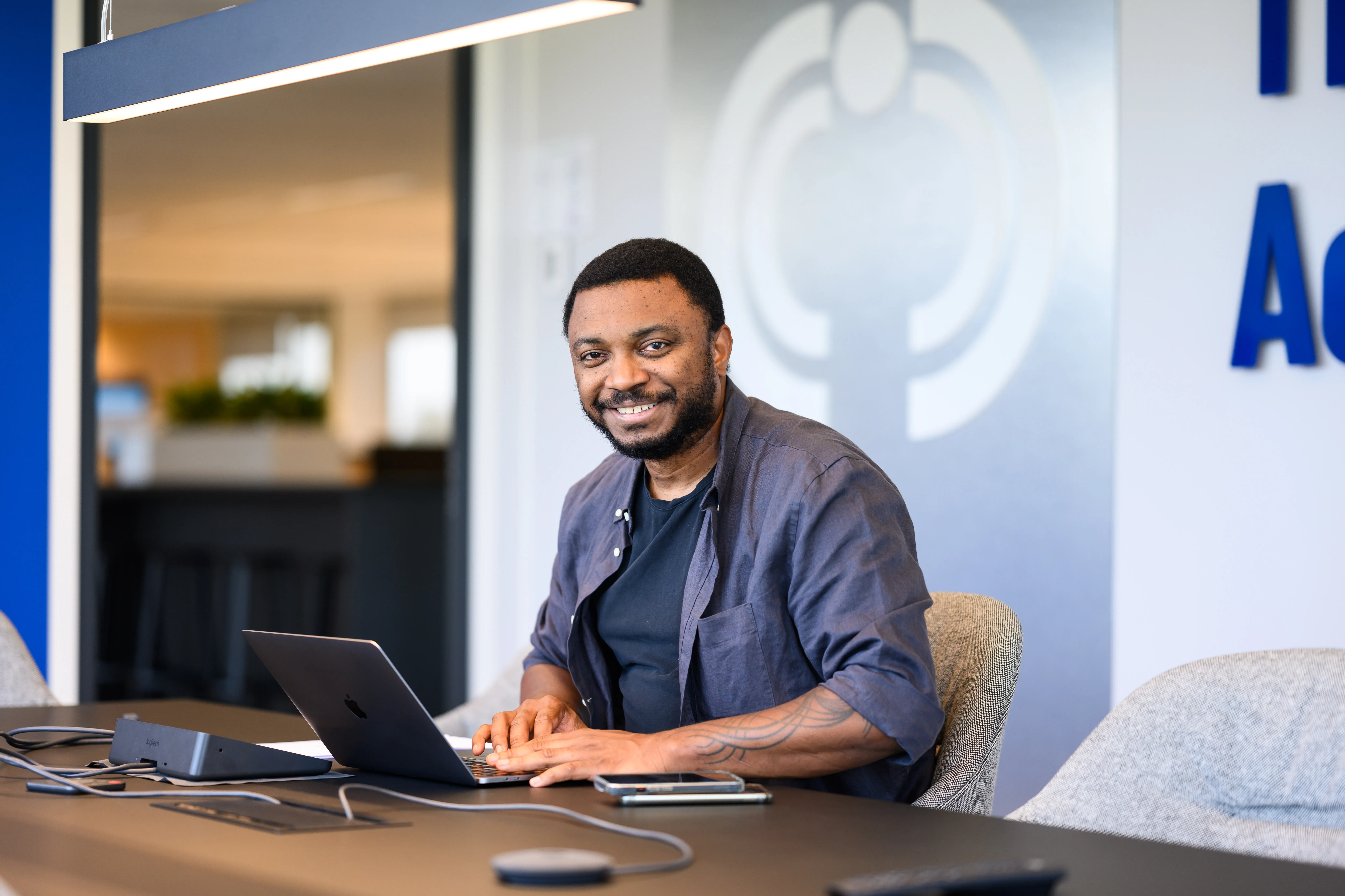 Smiling professional in a bright pink blazer working on a laptop in a modern, tech-savvy office.