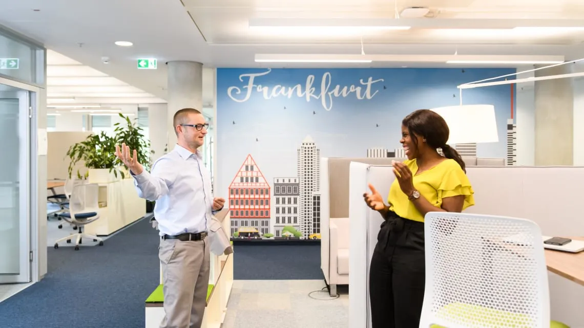 Zwei Kollegen unterhalten sich lachend in einem modernen Büro.