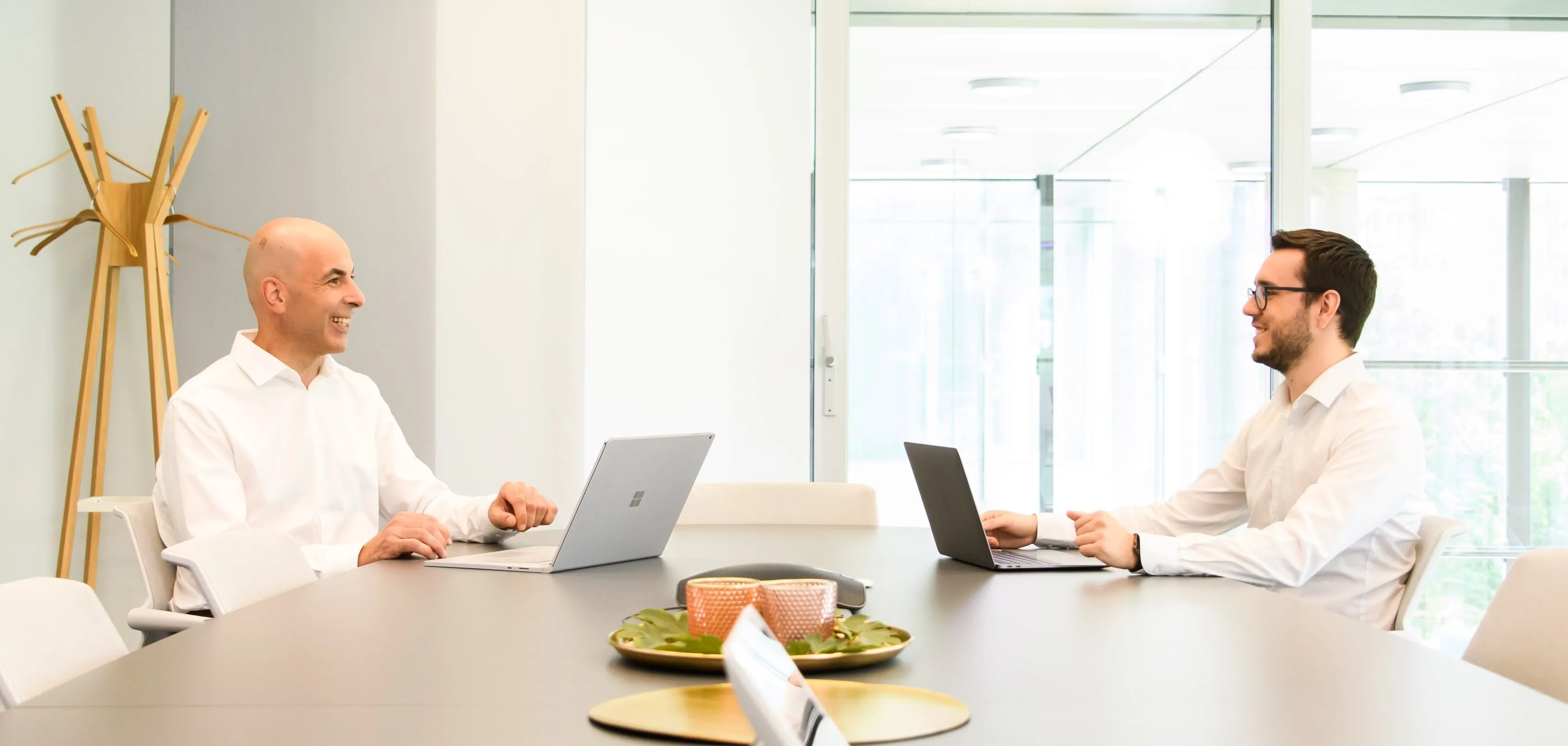 Zwei IT-Profis in einem modernen Konferenzraum, die sich lachend über ihre Laptops unterhalten.