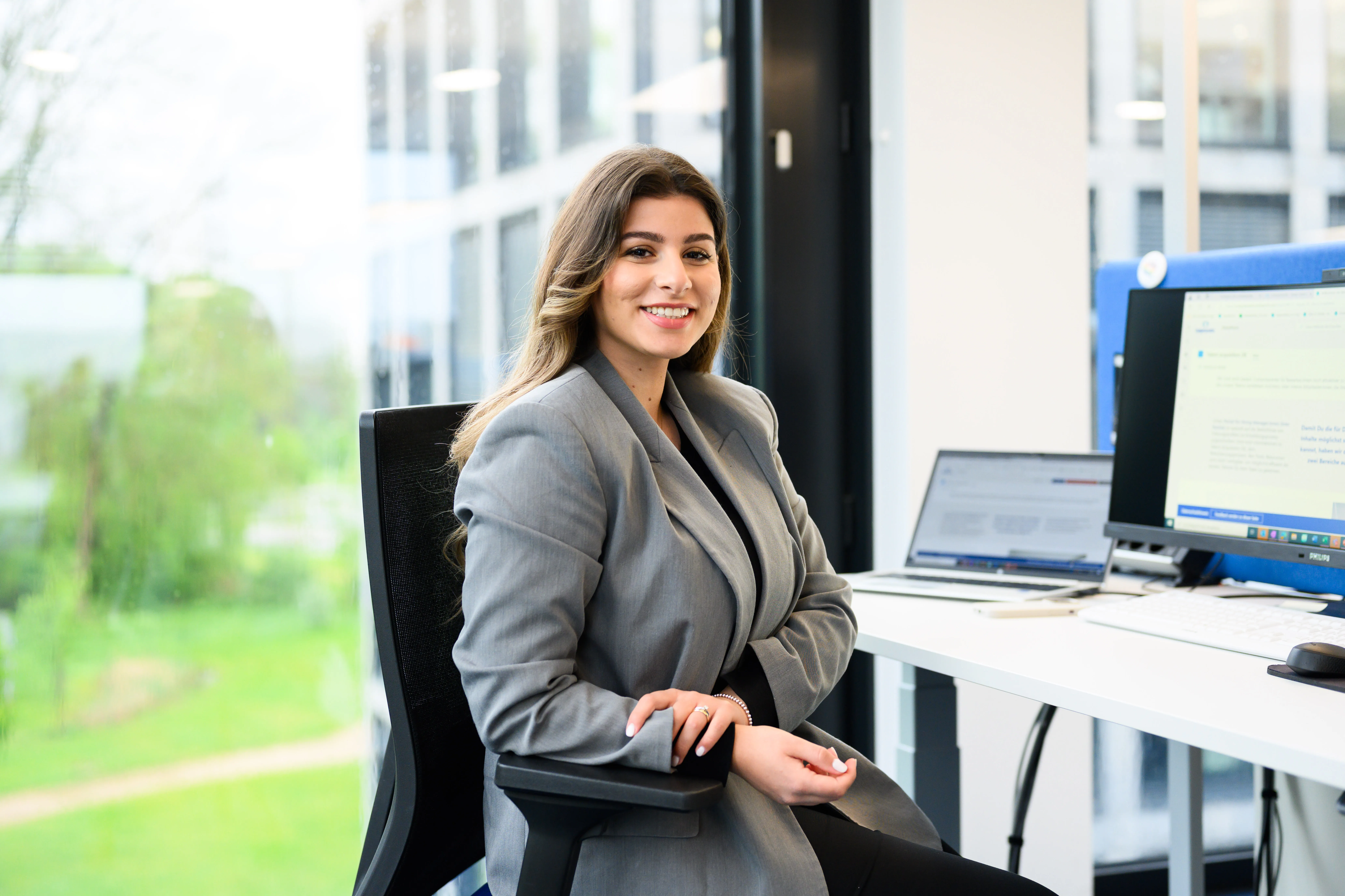 Smiling professional in a bright pink blazer working on a laptop in a modern, tech-savvy office.