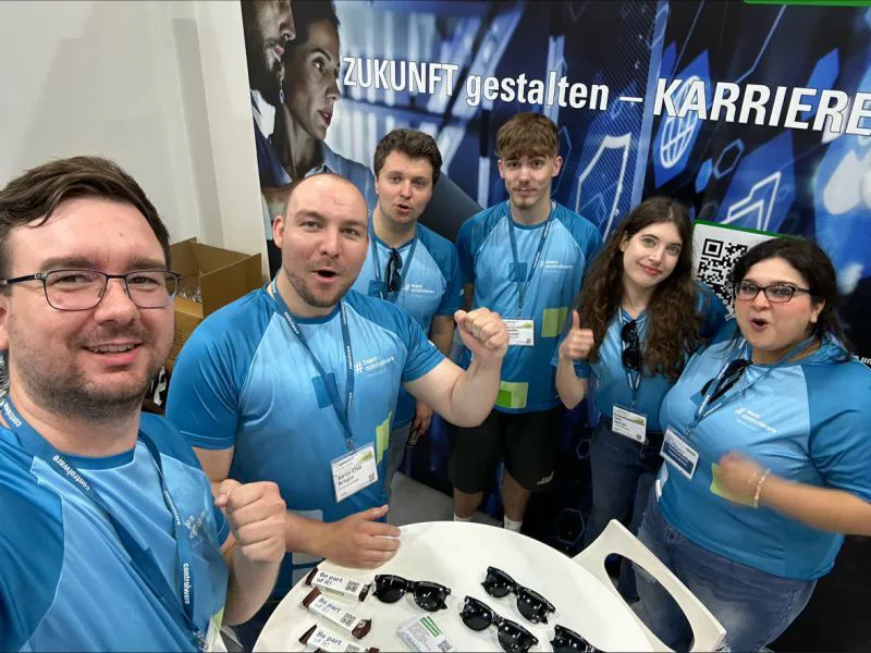 Sechs junge Menschen in blauen Team-Shirts motivieren dich am Karrierestand, gemeinsam die Zukunft zu gestalten.