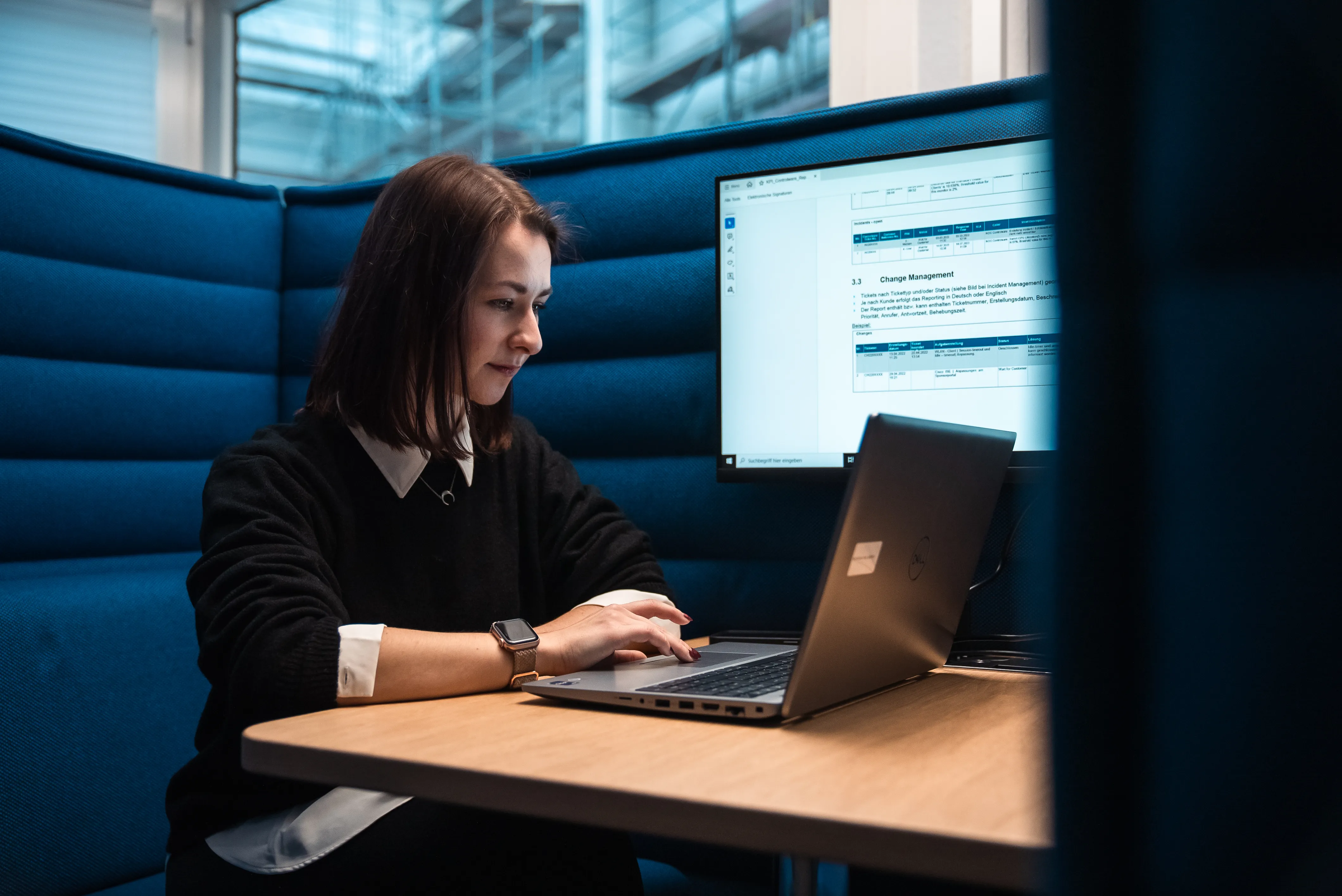 Junge Frau lächelt an einem Schreibtisch mit Laptop in modernem Büro – starte Deine Karriere in einem vielseitigen Umfeld.