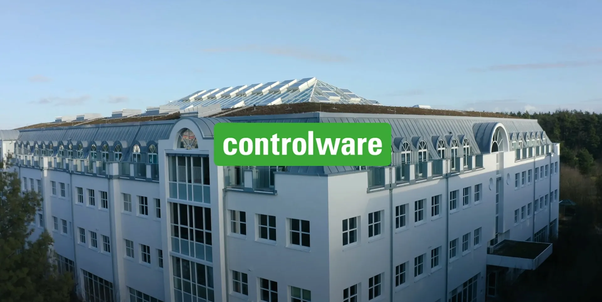Modernes Firmengebäude von Controlware mit Glasdach und grünem Logo, umgeben von Bäumen, bei Tageslicht.