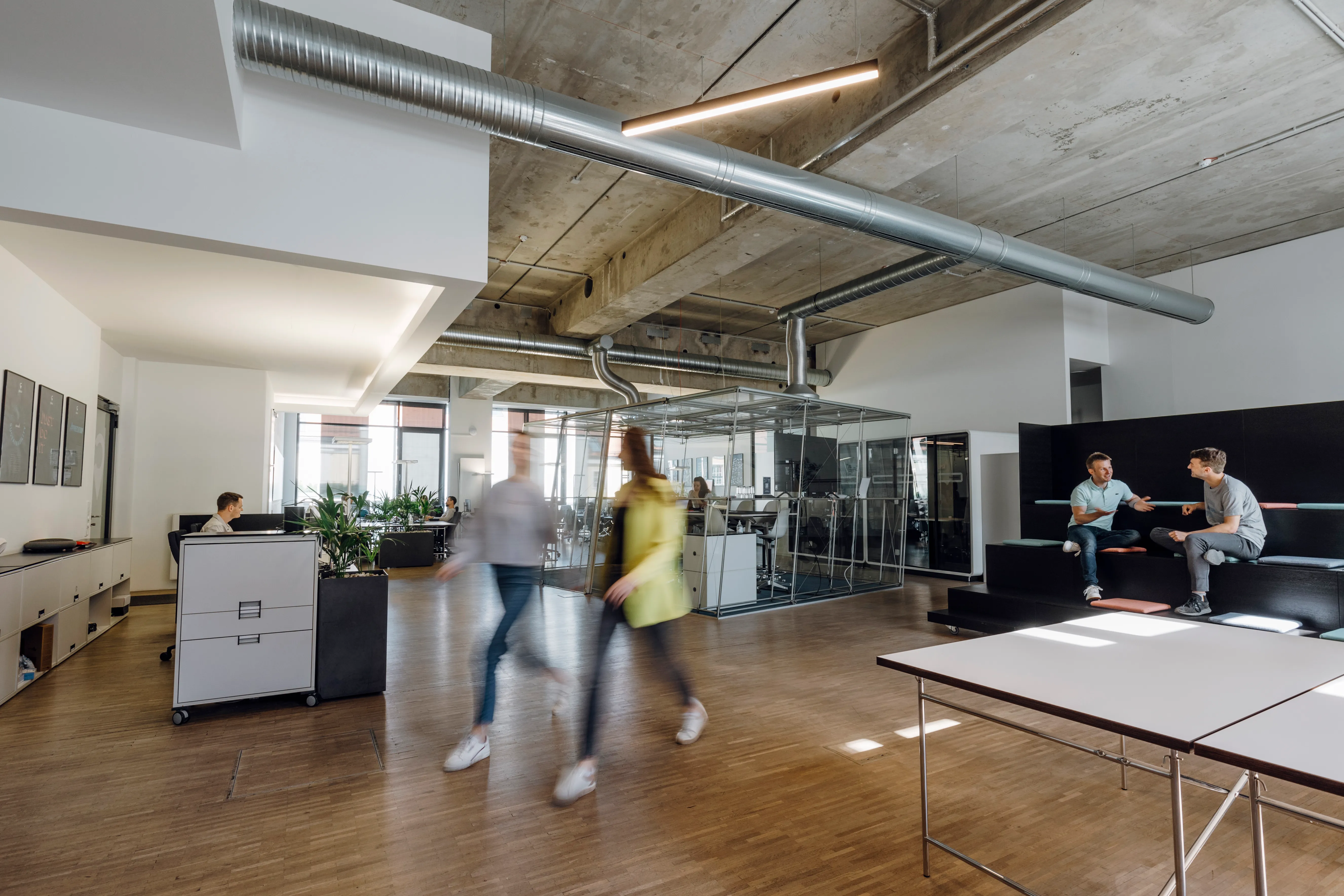 Modernes Büro von collaboration Factory GmbH mit offenen Arbeitsbereichen, Glaswänden und Kolleg:innen im Austausch.