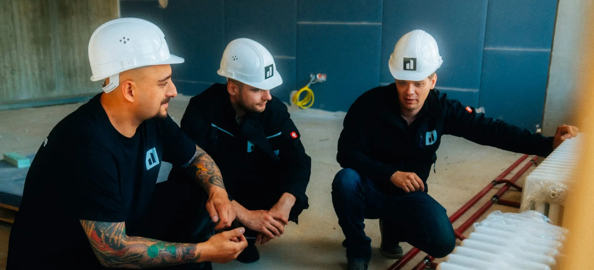 Drei Handwerker mit Helmen besprechen gemeinsam ein Projekt auf einer Baustelle.